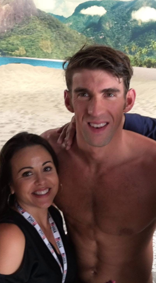 Two people smiling at the beach with mountains and a body of water in the background.