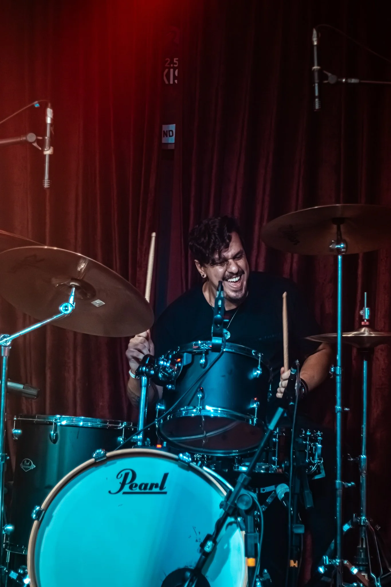 Drummer Francisco Nin playing drum set with intense expression, surrounded by microphones on stage.