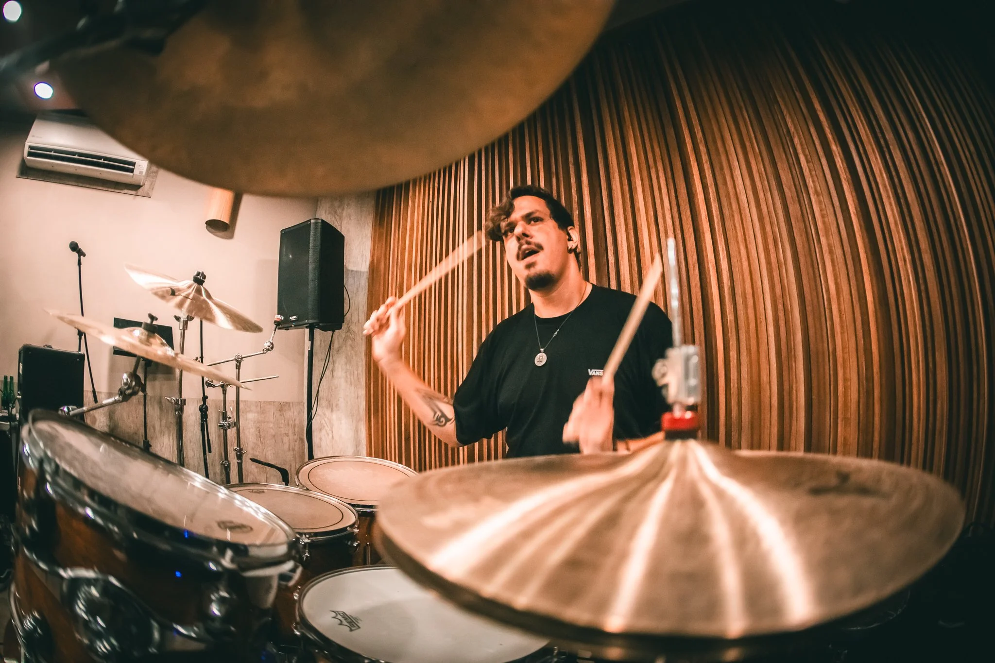 Drummer Francisco Nin playing drum set in a music studio with wood paneling.