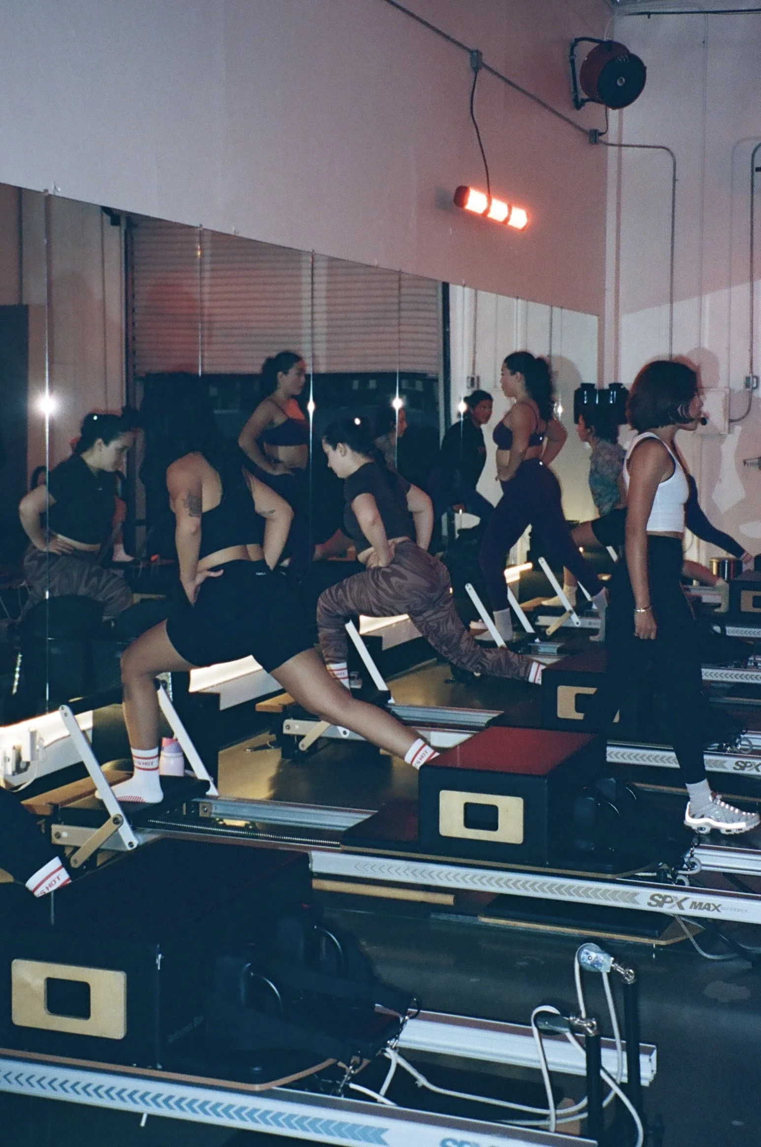 Group of women exercising on Pilates reformer machines in a fitness studio with mirrors and dim lighting.