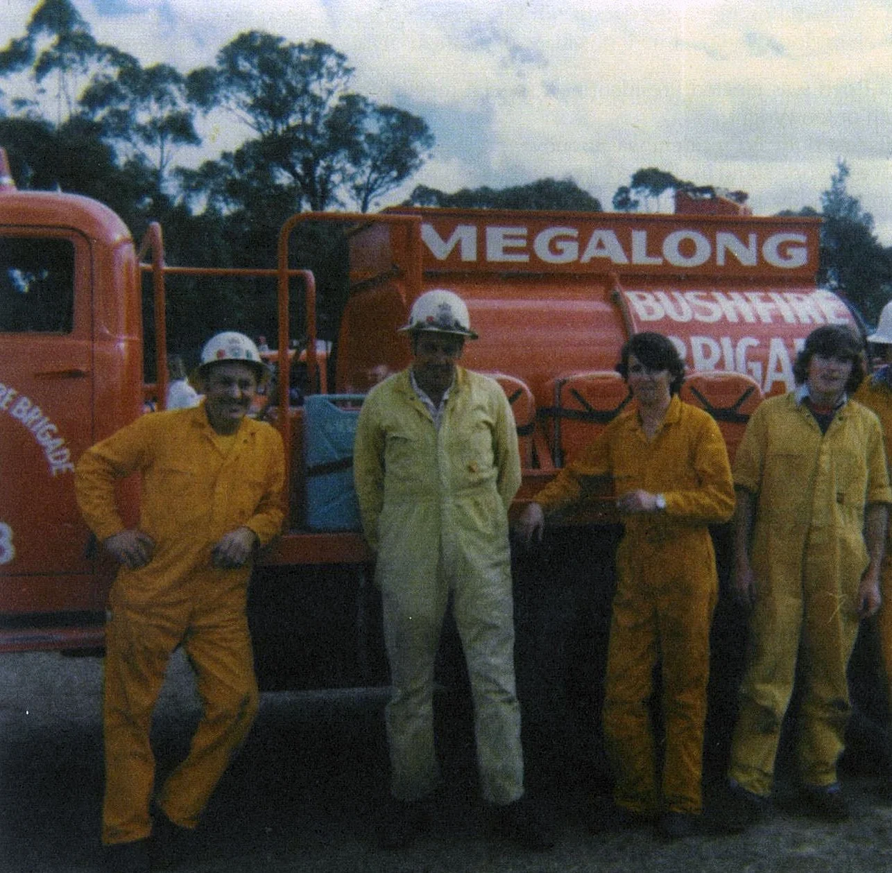 Four people in yellow jumpsuits and helmets standing in front of a red water truck labeled "MEGALONG Bushfire Brigade."