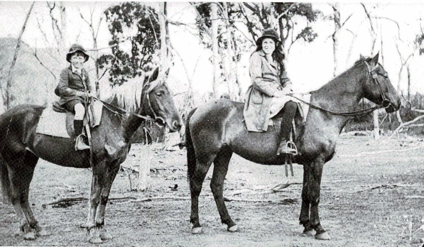 Two women riding horses outdoors in a wooded area, dressed in early 20th century clothing. Megalong Valley.