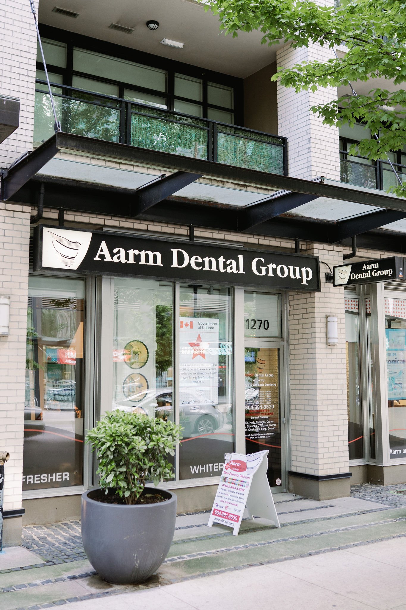 storefront of Aarm Dental Group with a black sign, large glass windows, and a potted plant outside.