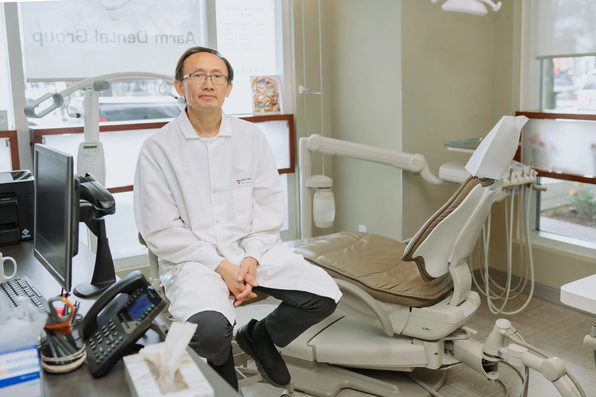 A male doctor sitting on a stool in a dental office.