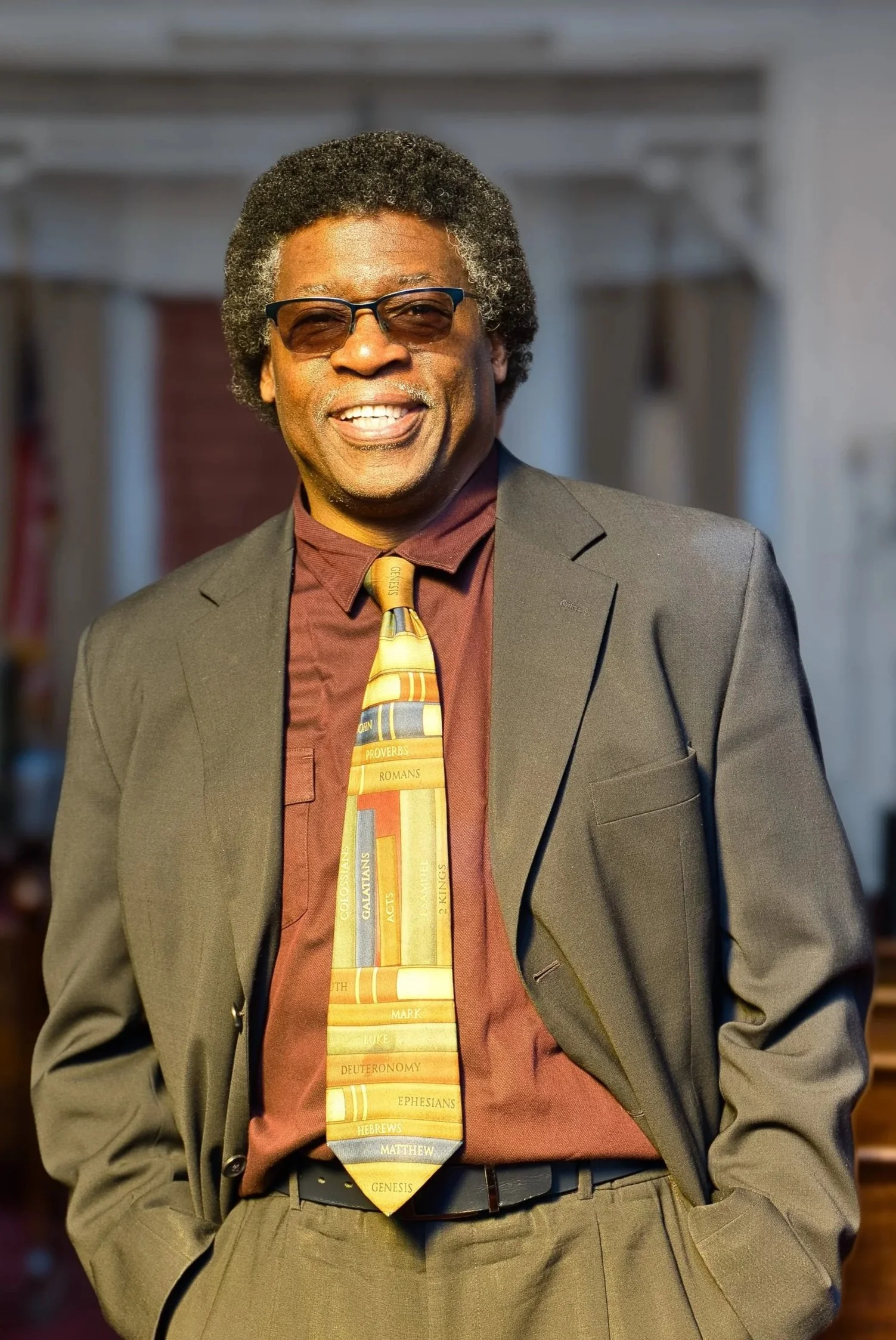 Professional portrait headshot of a black businessman in a suit with both his hands in his pockets with his tie exposed