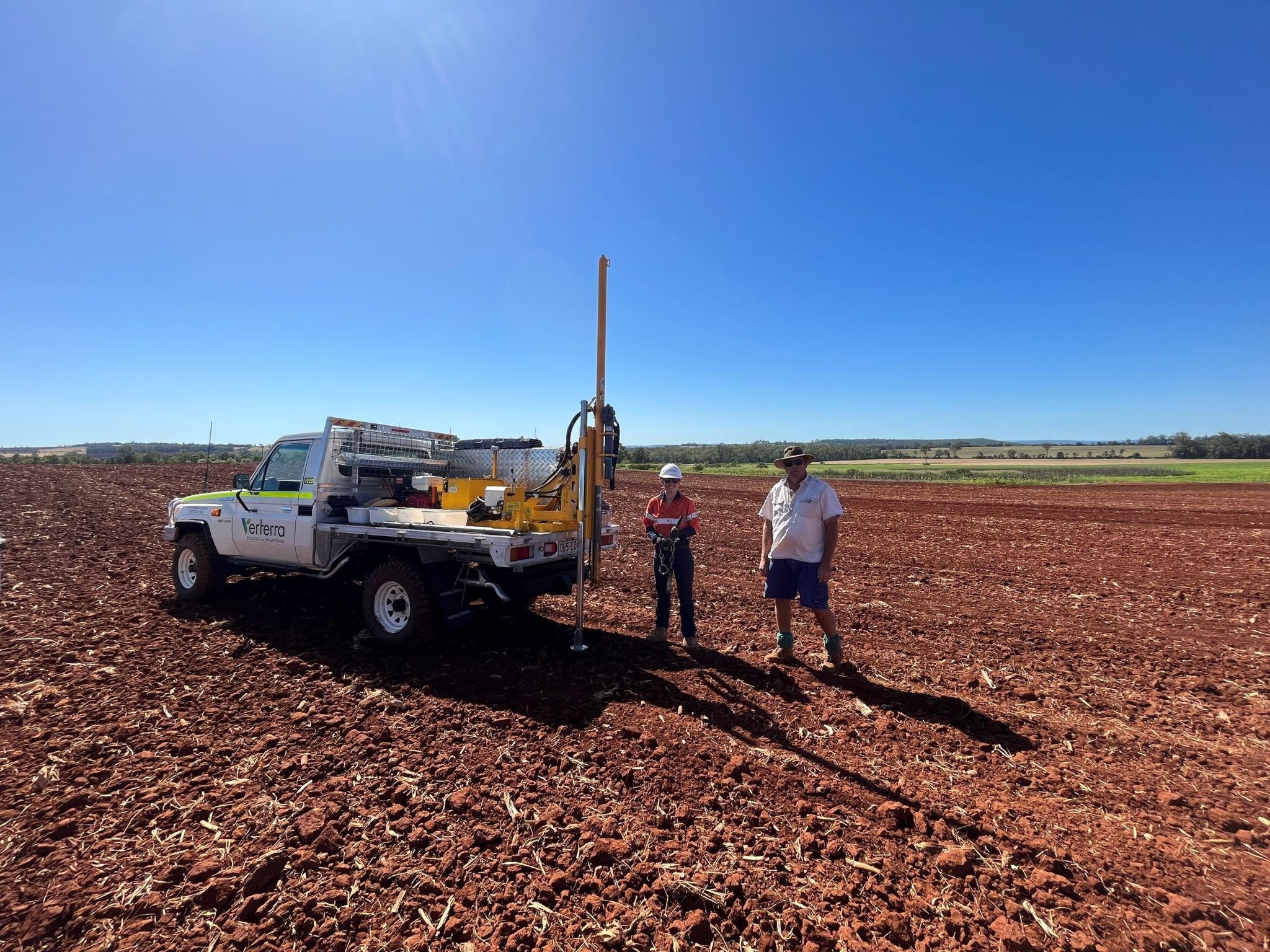 Two people in a ploughed paddock with a soil sampling rig
