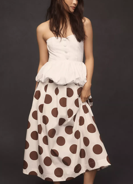 Woman in a strapless white top and polka dot skirt, styled in classic fashion against a dark background.