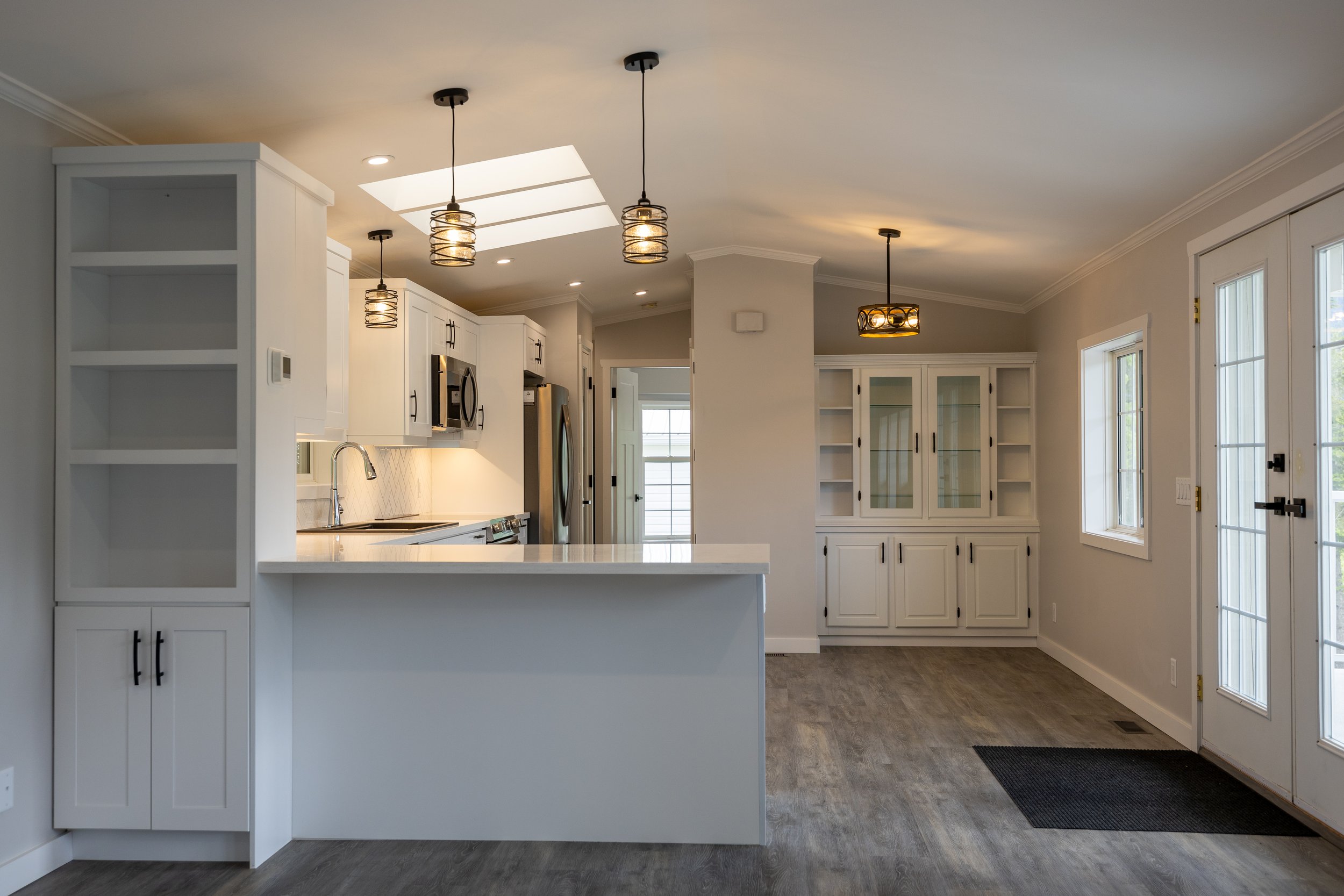 Kitchen with white cabinetry, stainless steel appliances, pendant lights, skylight, and a dining area with shelving and windows.