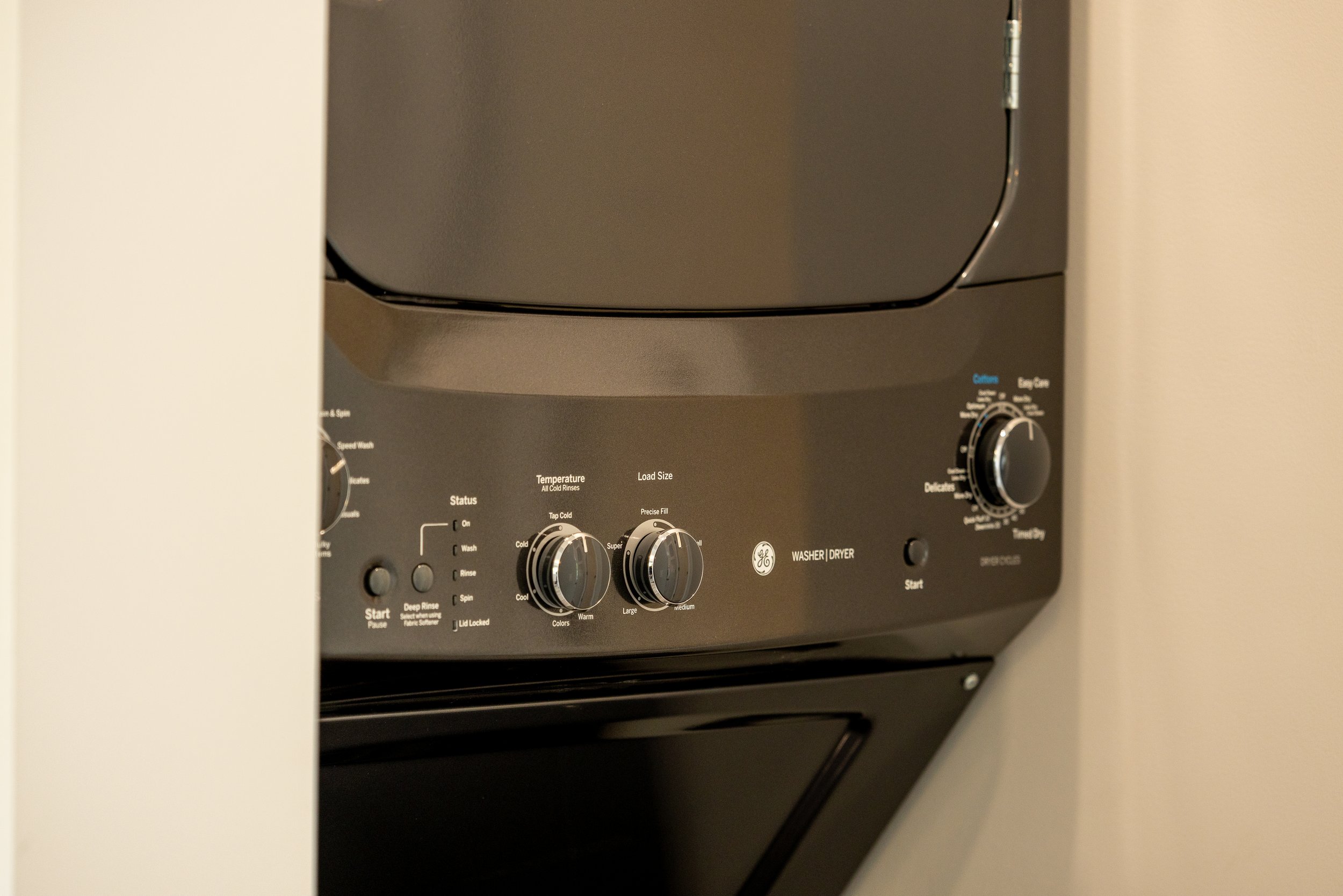 Close-up of a black GE washer and dryer stacked in a laundry area, with control knobs and start buttons visible.