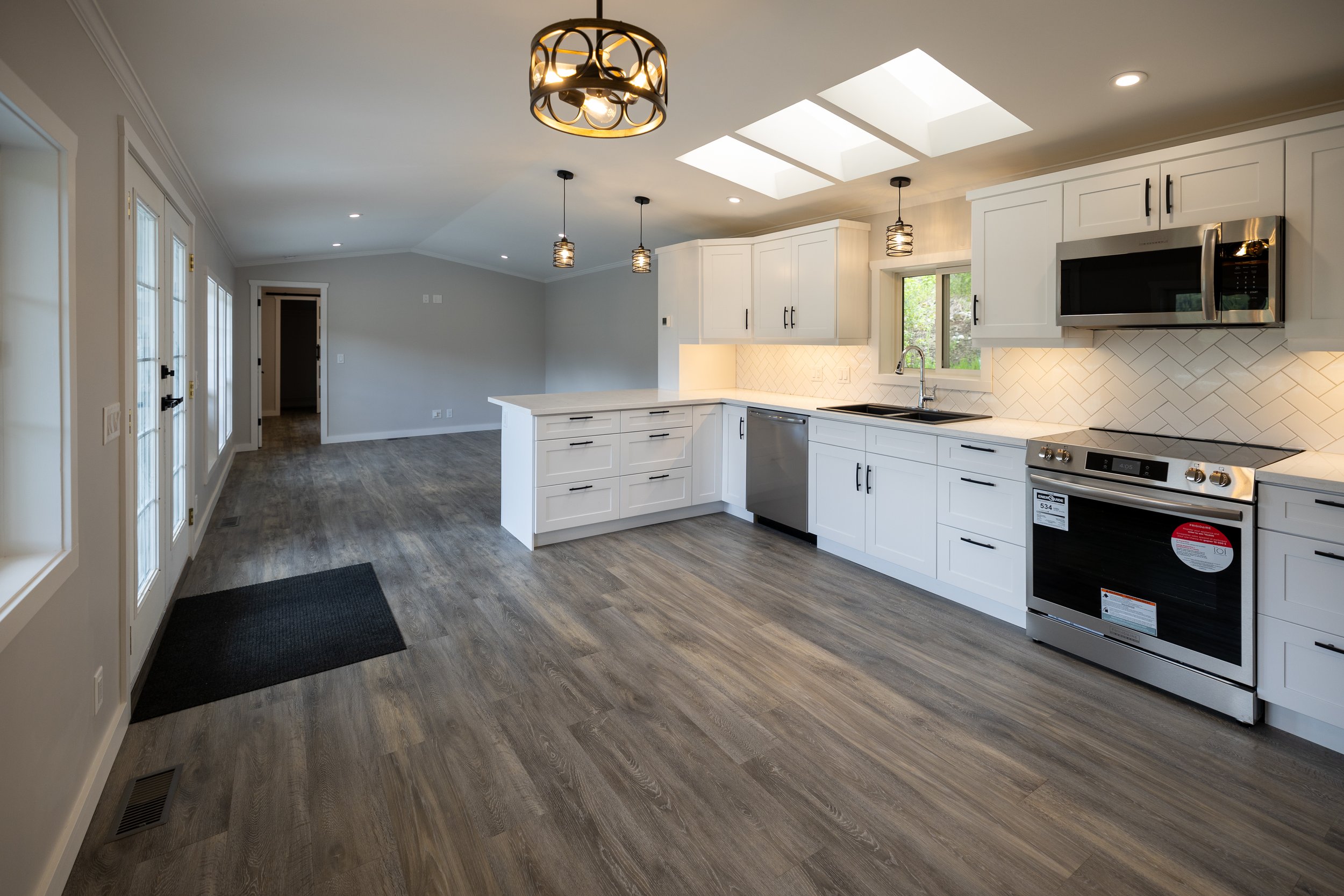 Modern kitchen with white cabinets, stainless steel appliances, wooden floors, and skylights.