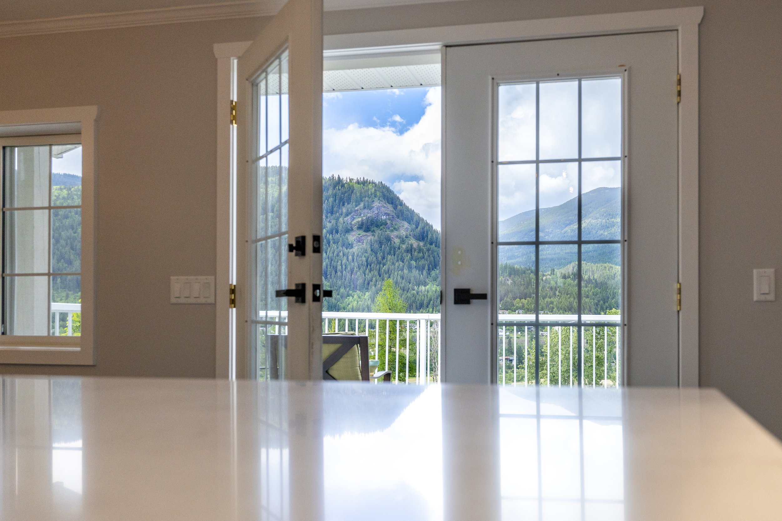 View through glass double doors onto mountain landscape with green trees and blue sky.