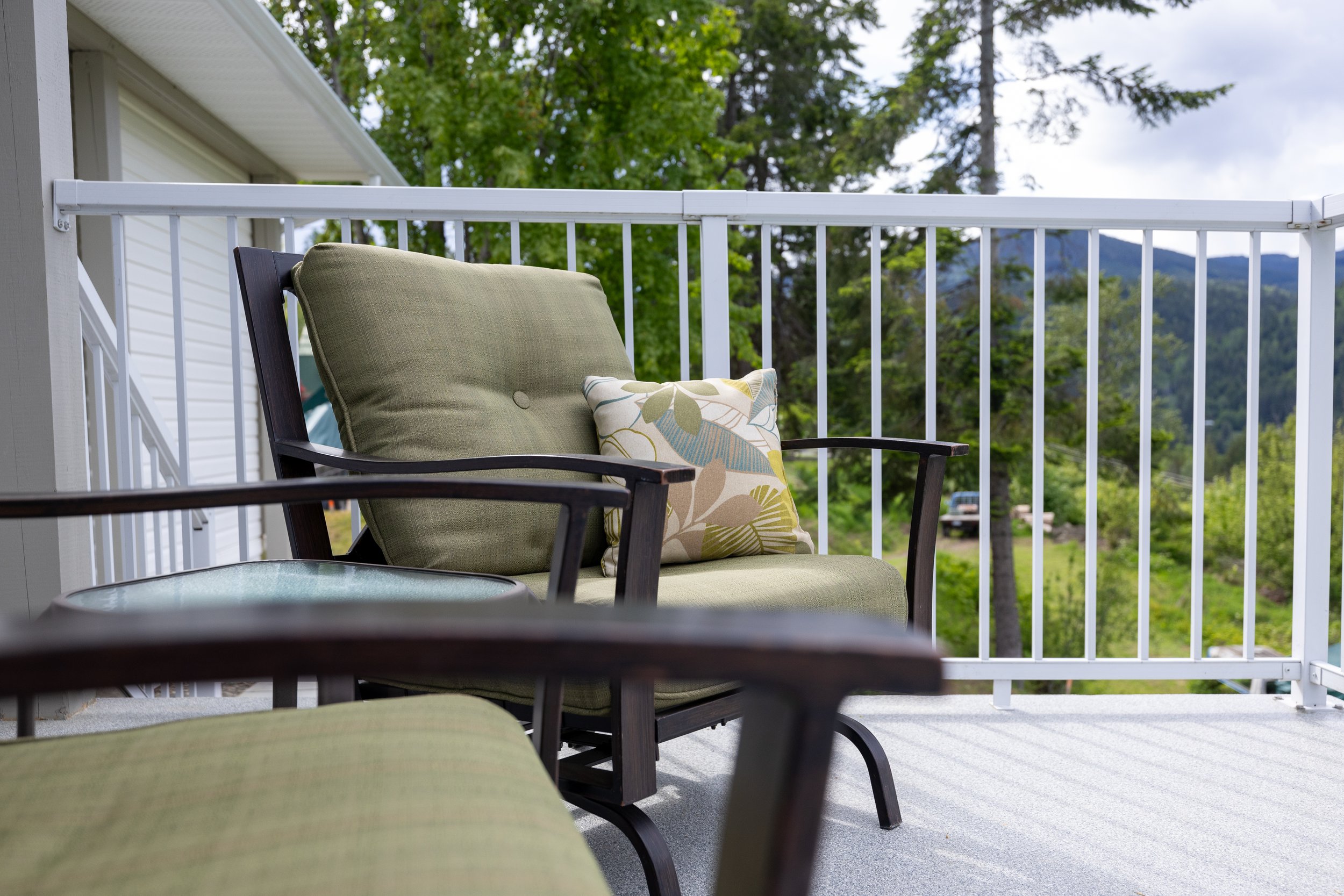 Patio furniture on a balcony with a cushioned chair, a pillow, and a view of trees and distant mountains.