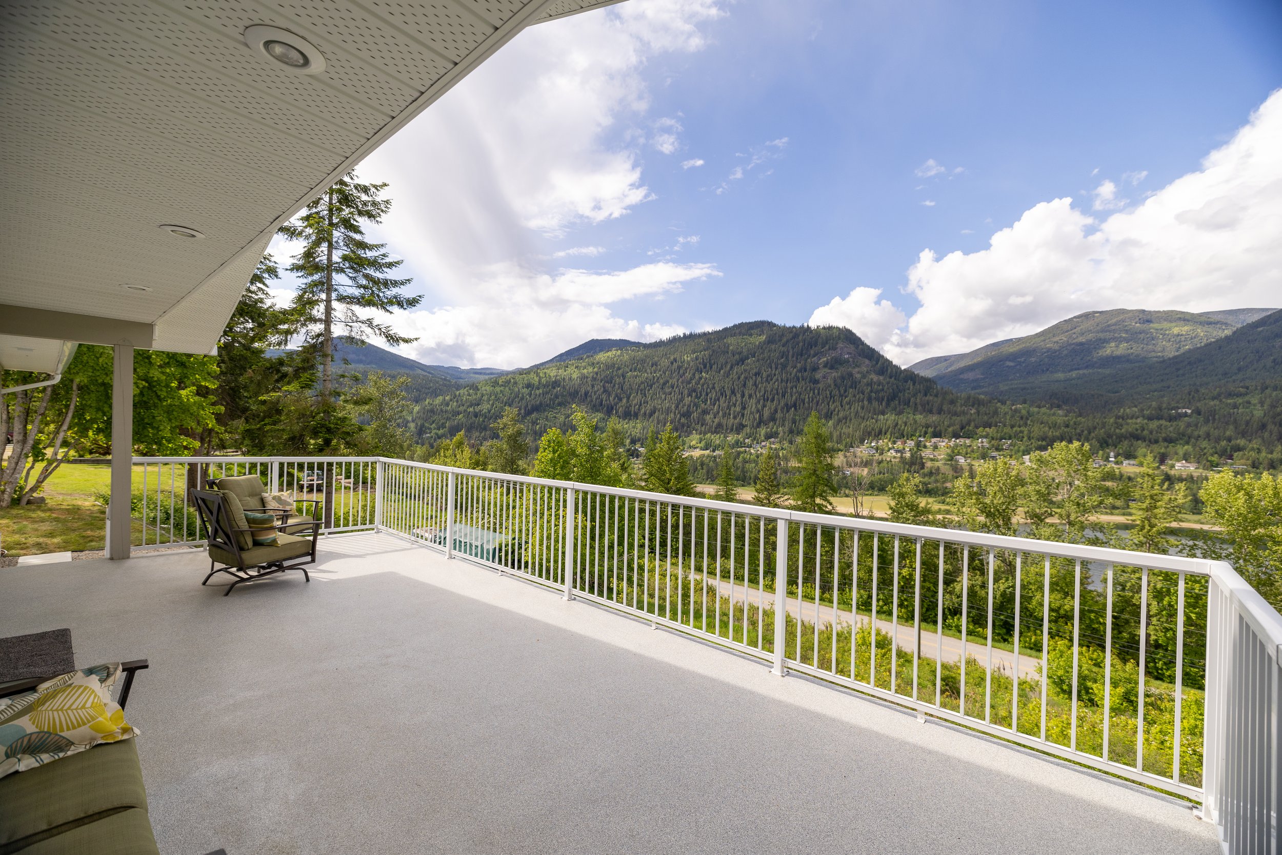 Balcony overlooking a lush green valley and mountains under partly cloudy sky.