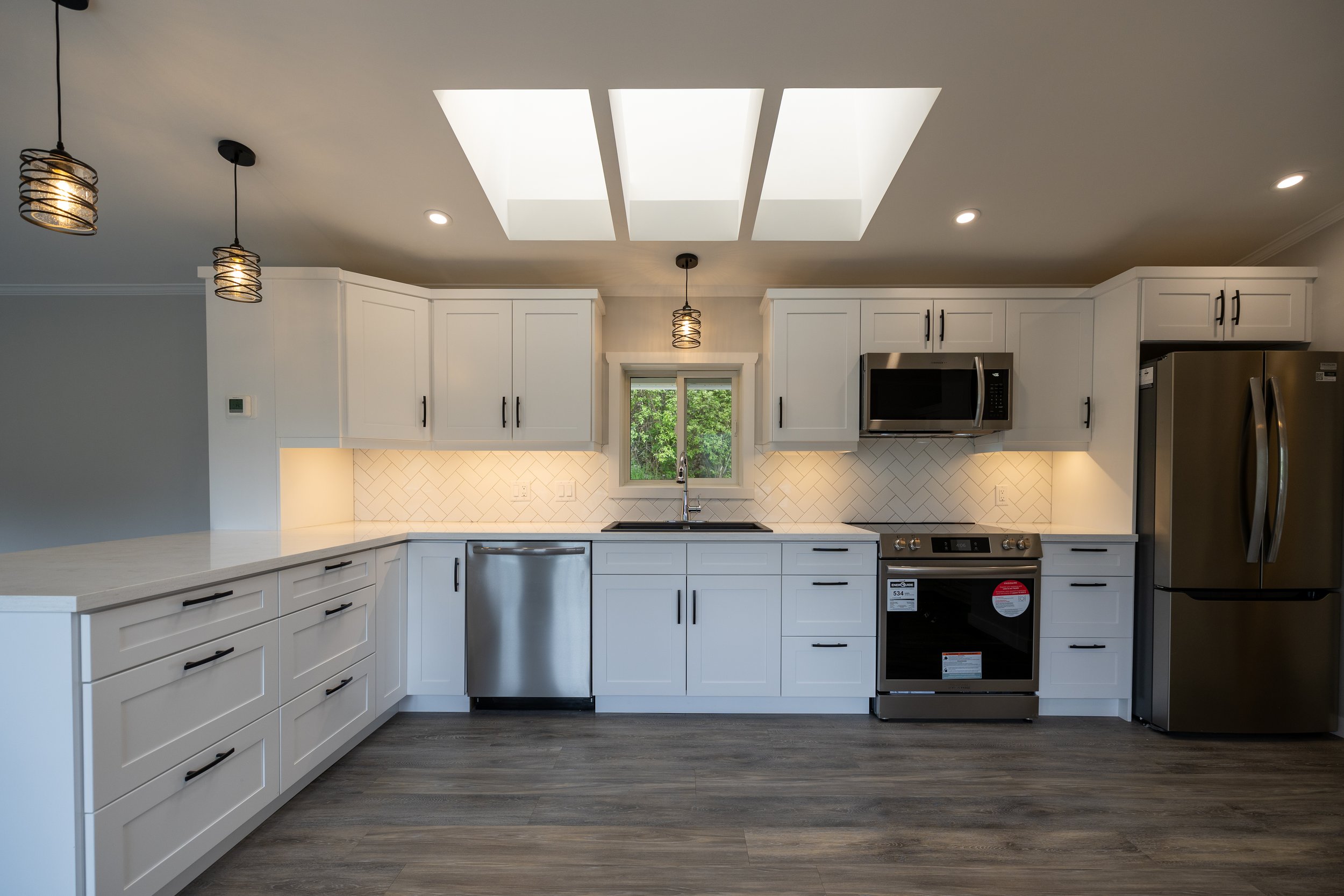 Modern kitchen with white cabinets, stainless steel appliances, pendant lights, and a skylight.