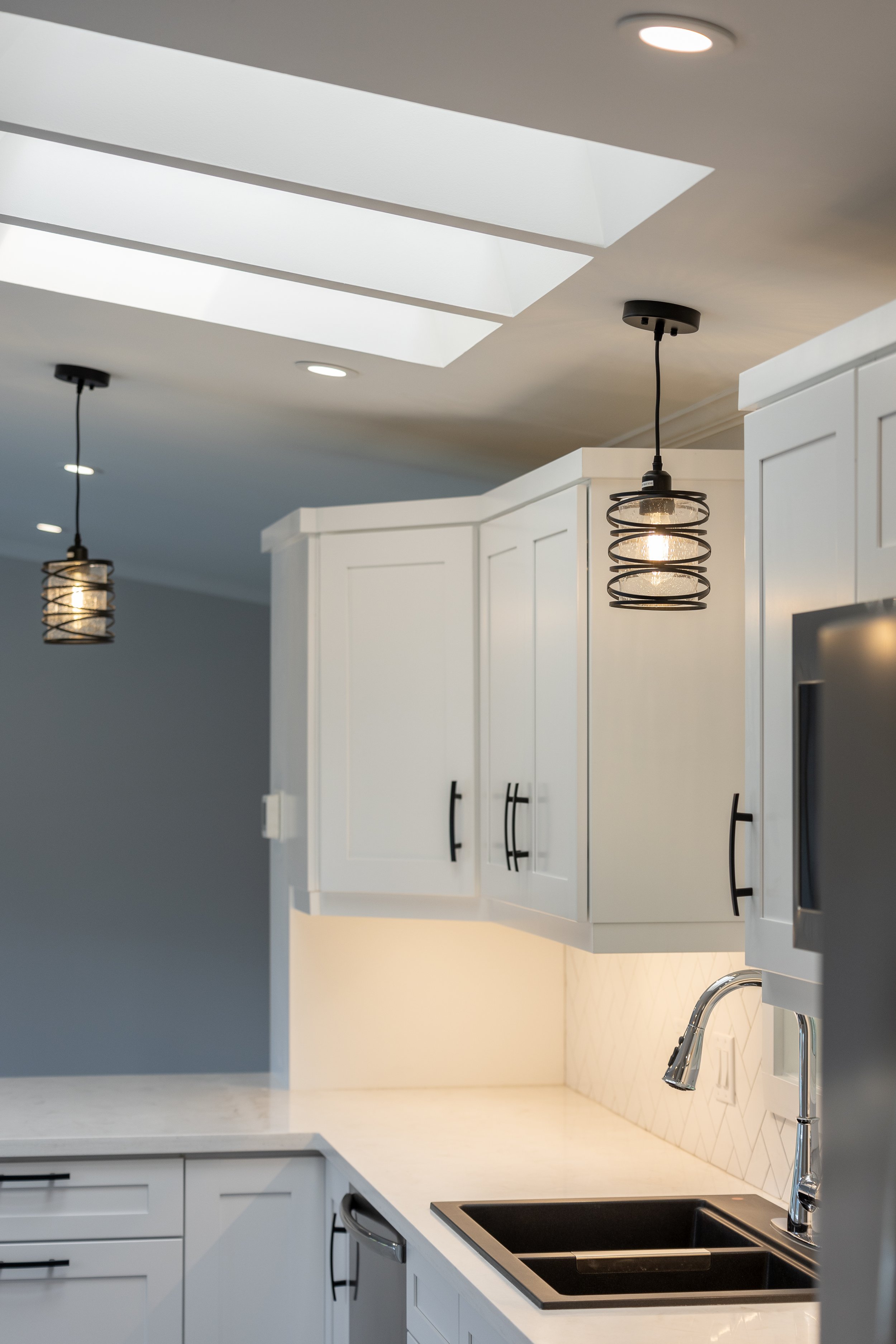 Modern kitchen with white cabinets, black sink, granite countertops, and decorative pendant lights.