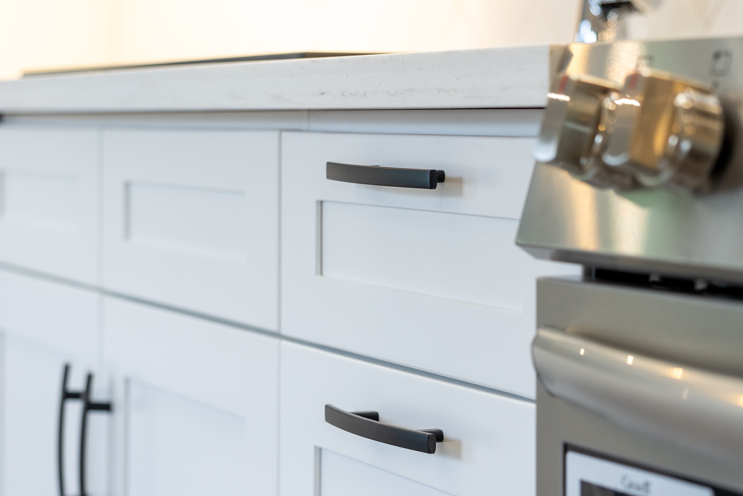 White kitchen cabinets with black handles next to a stainless steel oven and stove.