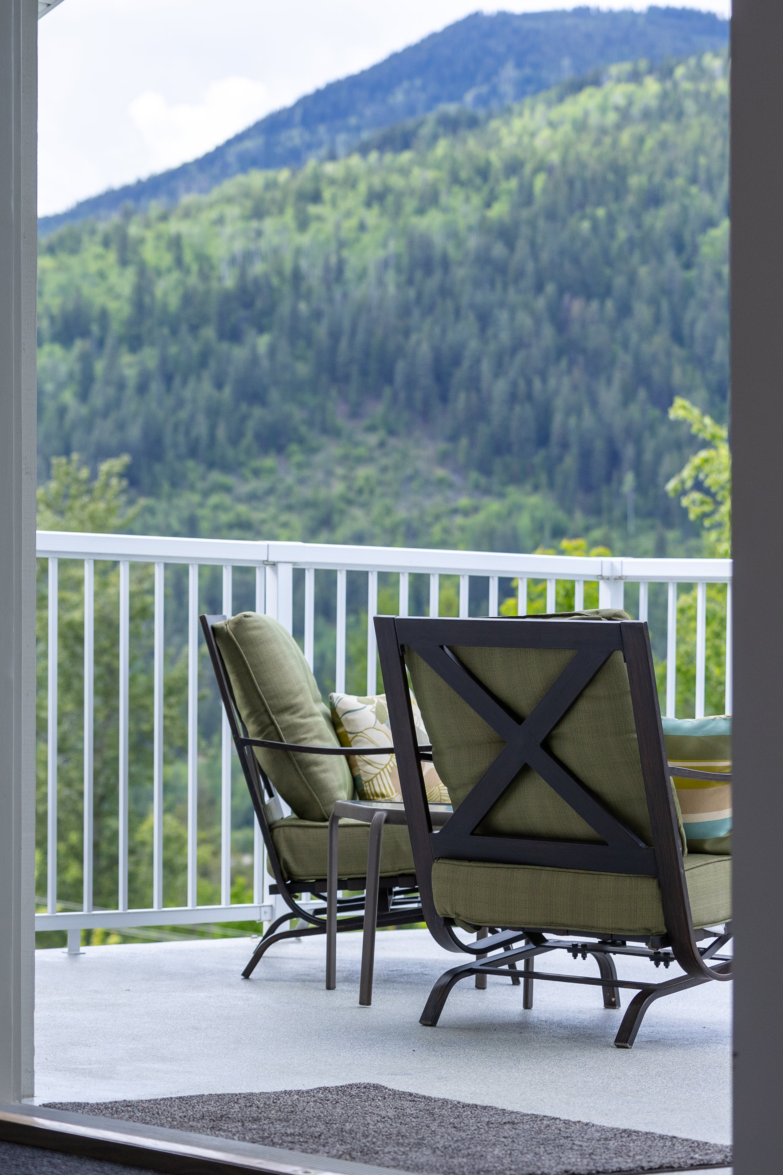 Outdoor balcony with green cushioned chairs overlooking lush green mountains.