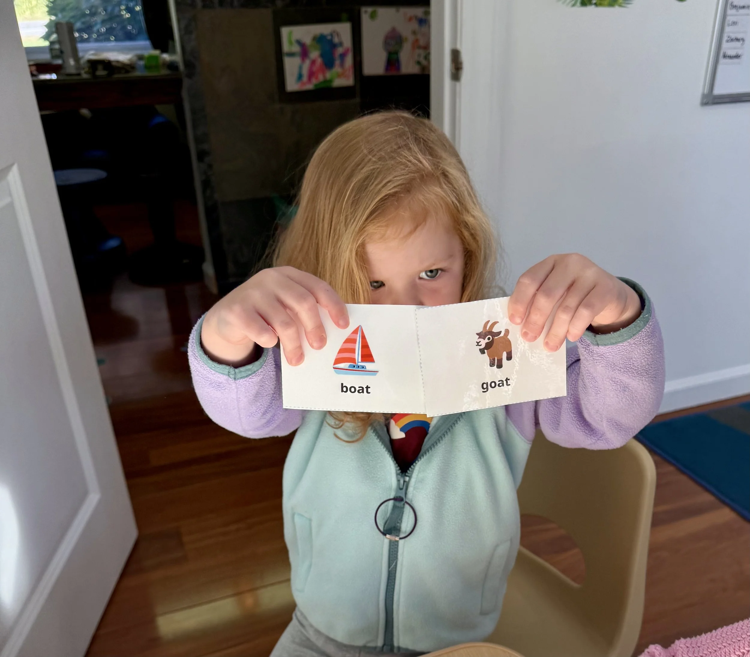 Preschooler smiling tPreschooler holding up rhyming picture cards during small group literacyhrough a magnifying glass