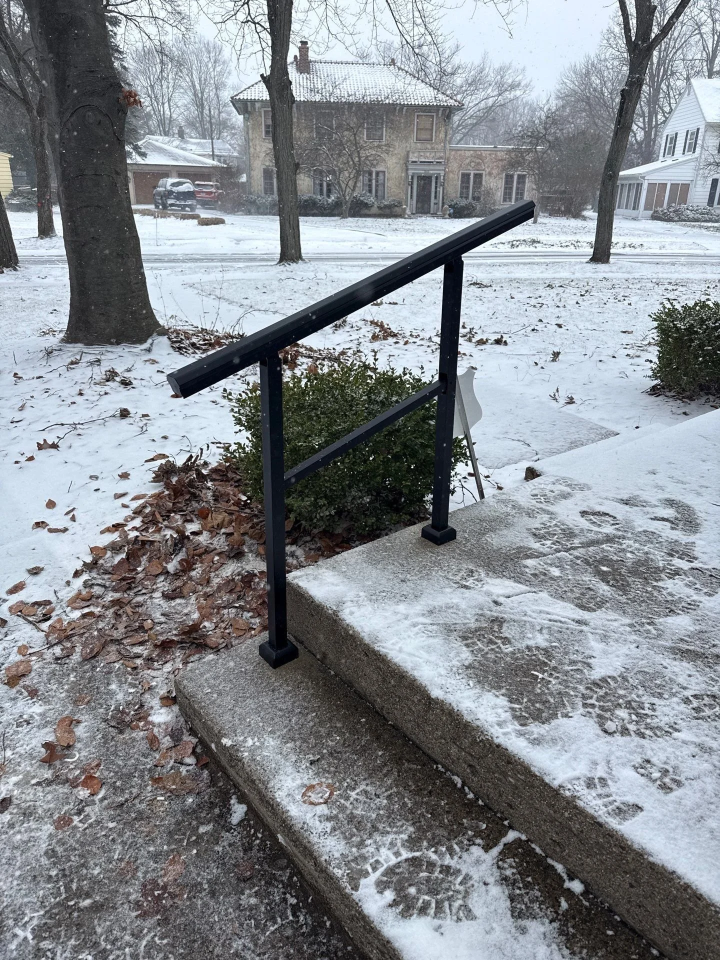 Wobbly front porch railing repair completed by Rob’s Handyman Service in South Bend, Indiana, featuring a newly installed black metal handrail on concrete steps during winter weather.