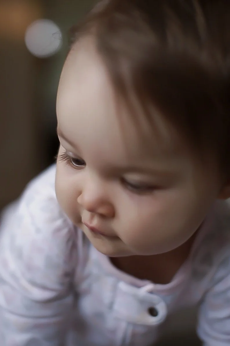 Close-up of a young child with brown hair and light skin, looking down and slightly to the side, wearing a white shirt.