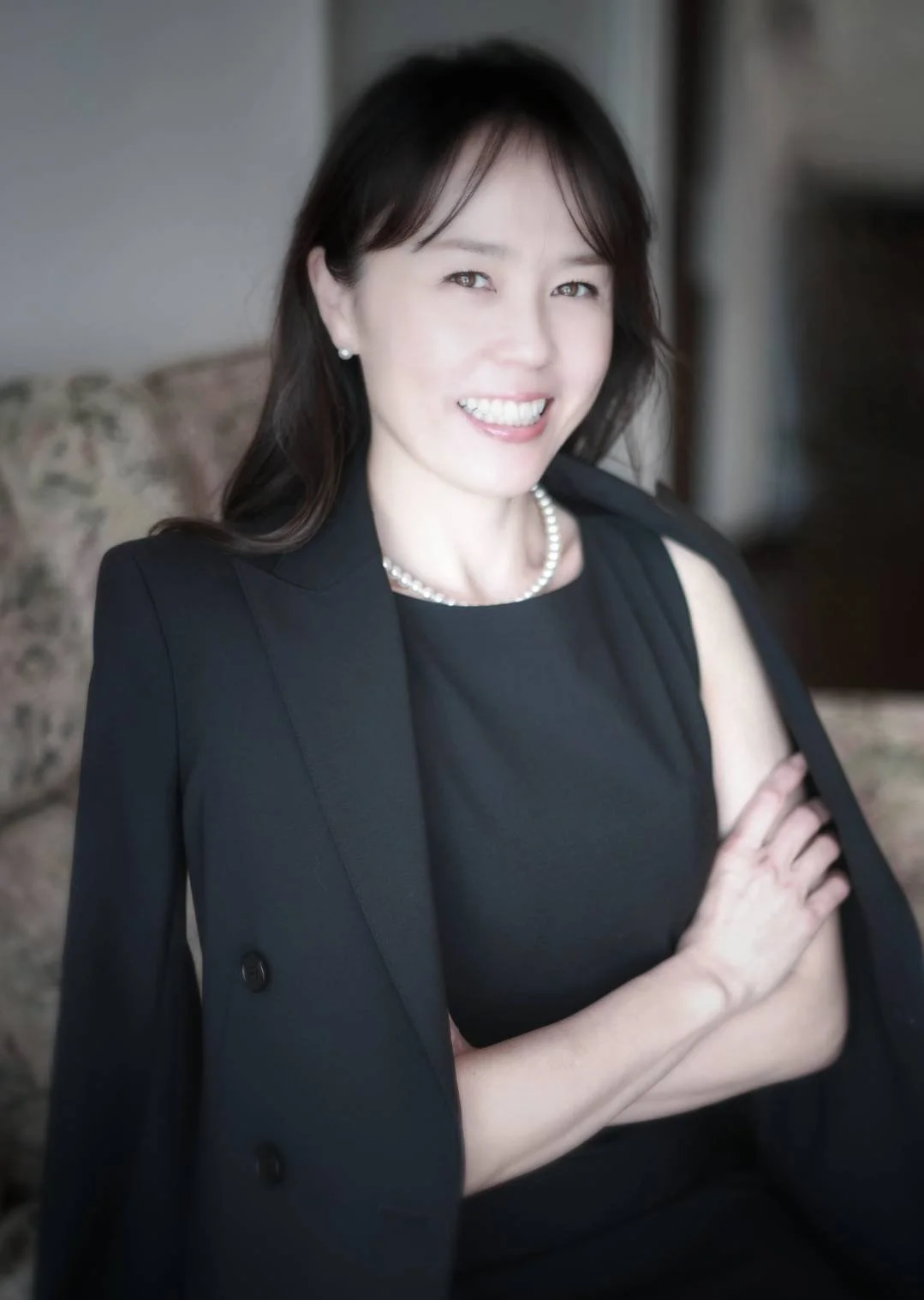 黒いドレスとジャケットを着た女性が微笑みながらポーズをとる。