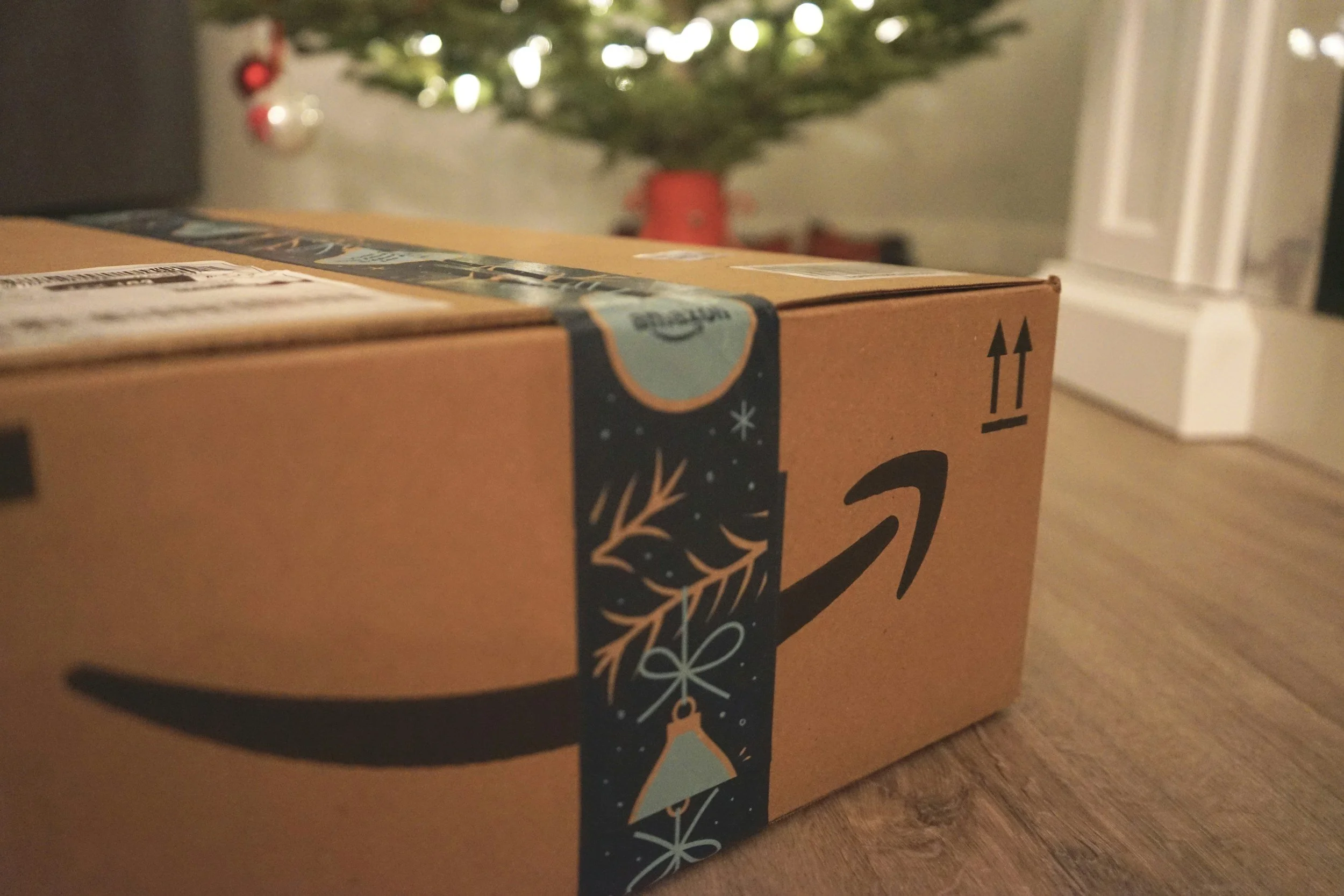 Amazon package with holiday-themed tape in front of a decorated Christmas tree.