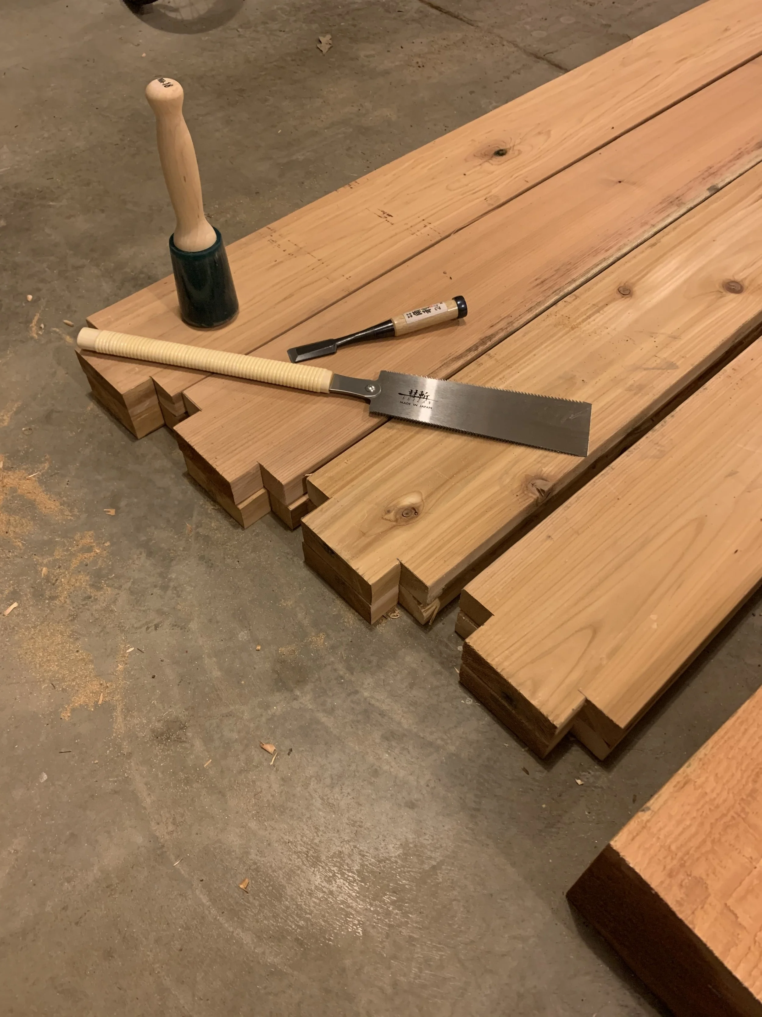 Wooden planks on the floor with a hand saw, hammer, and chisel placed on them.