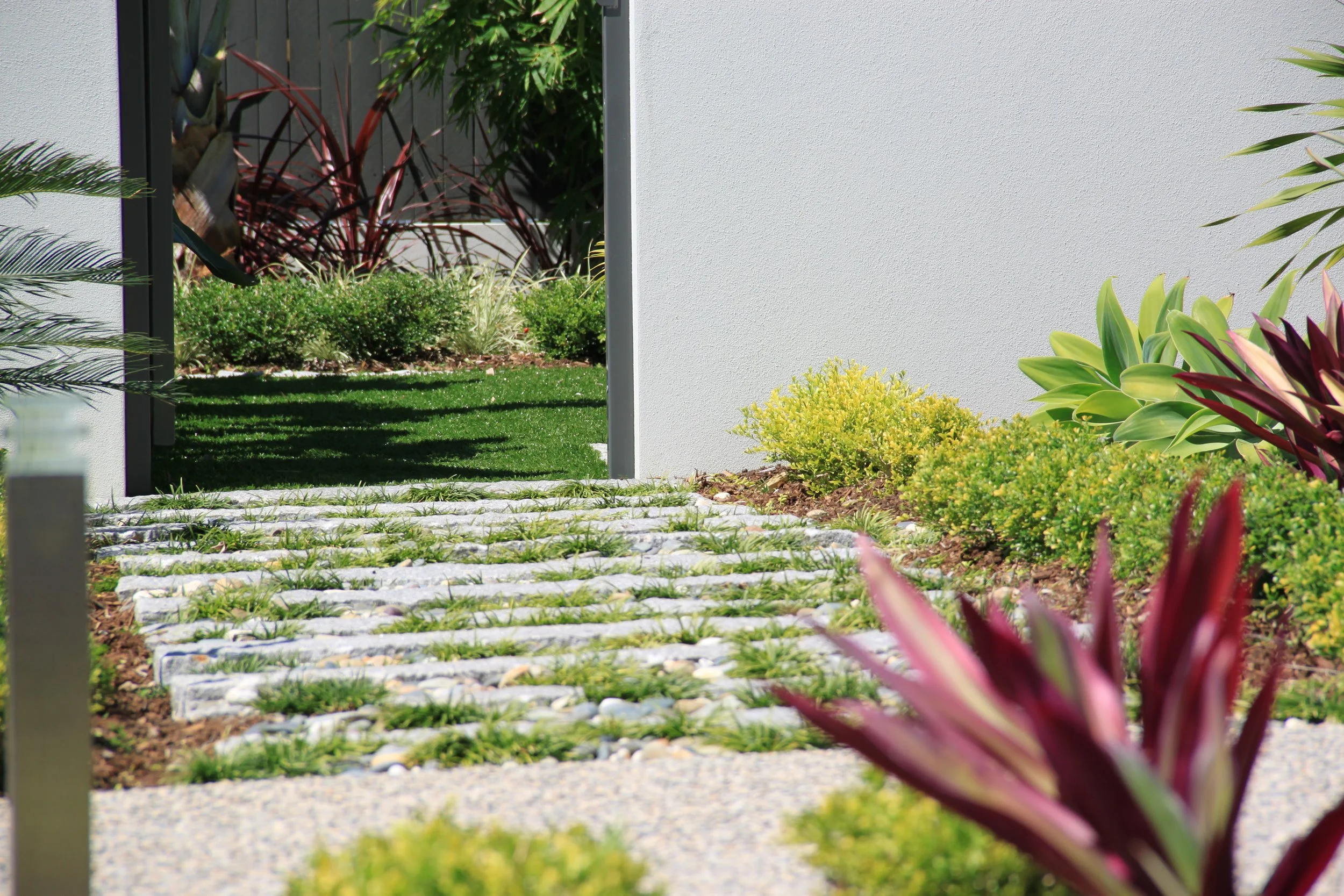 Modern garden with a stepping stone path surrounded by green foliage and colorful plants.