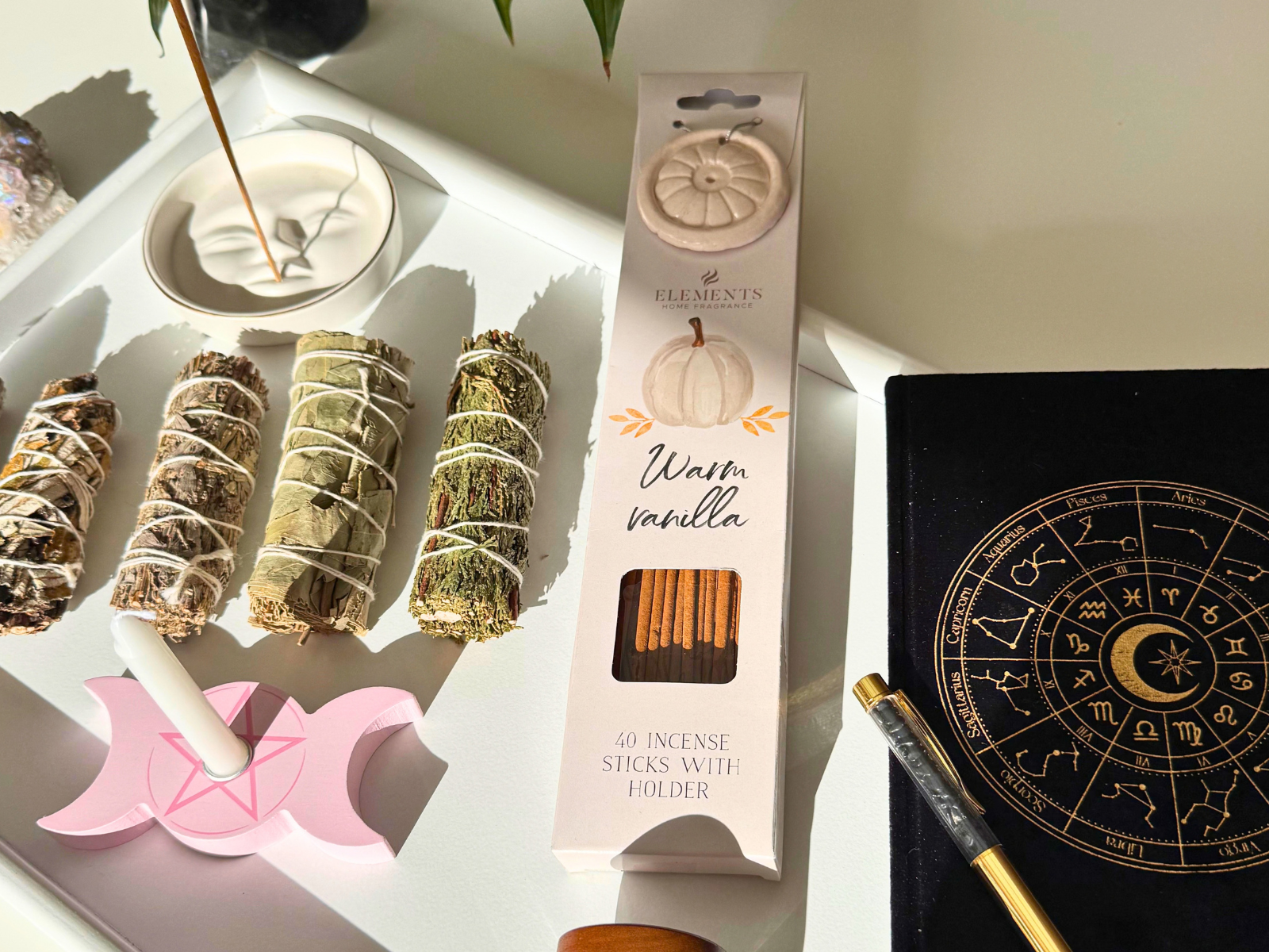 Incense, smudge, spell candle, bath salts and astrology journal laid out on a white tray