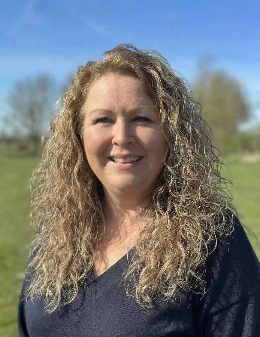 Smiling woman with curly blonde hair in an outdoor setting.