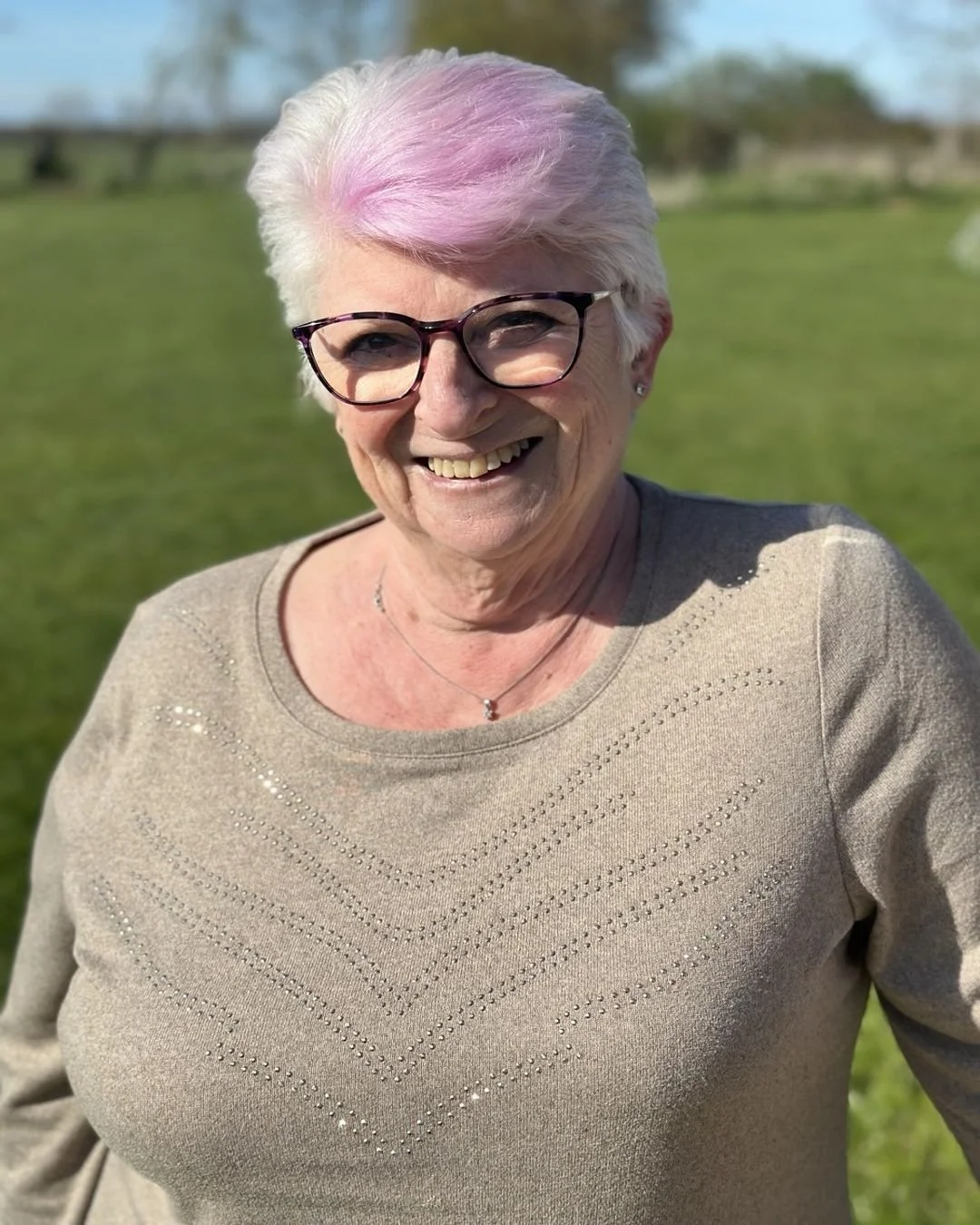 A smiling woman with short, styled gray hair and pearl earrings, wearing a dark top and a pearl necklace.