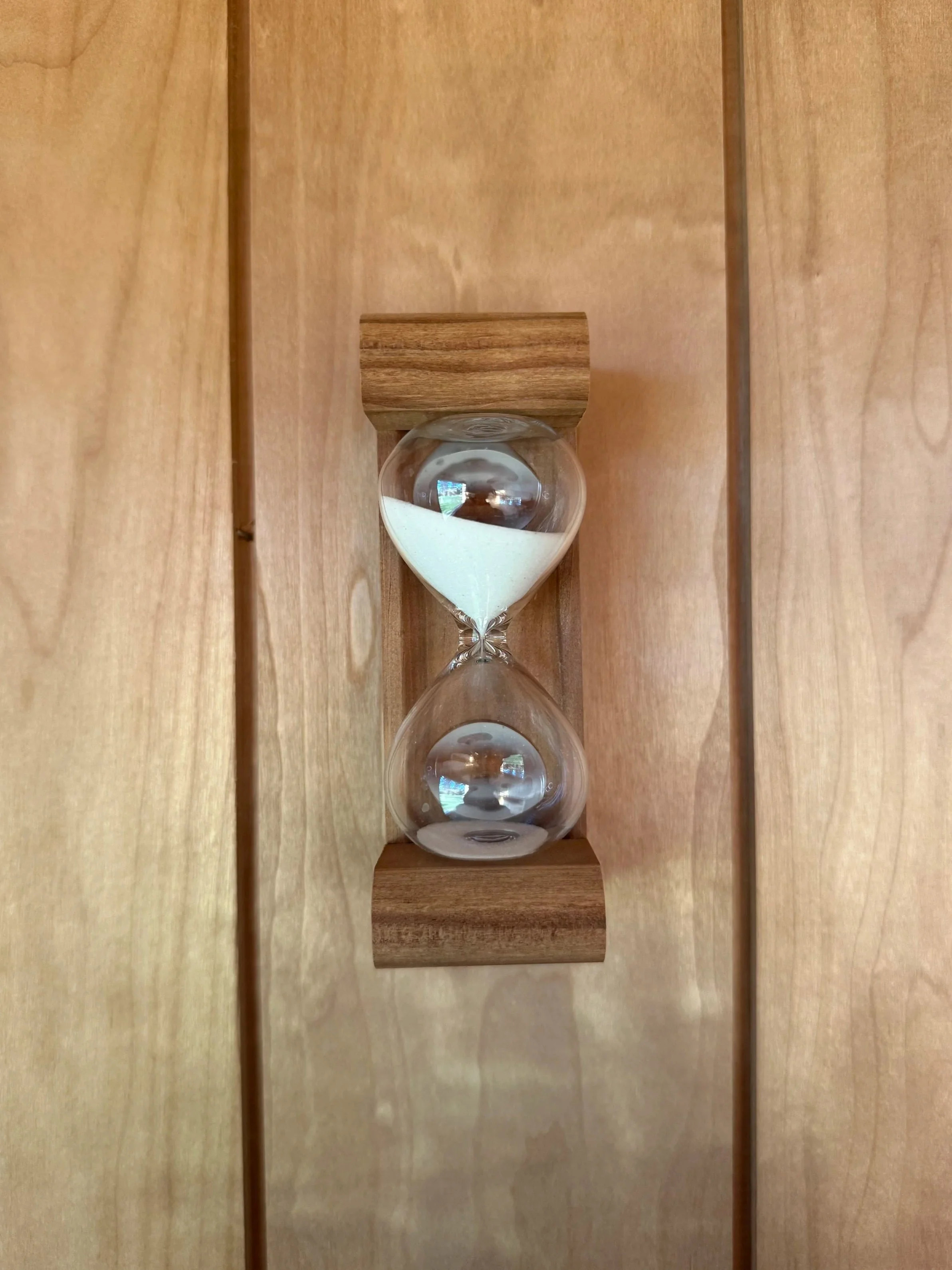 An hourglass with the top half filled with white sand and the bottom half empty, placed between wooden blocks on a wooden surface.