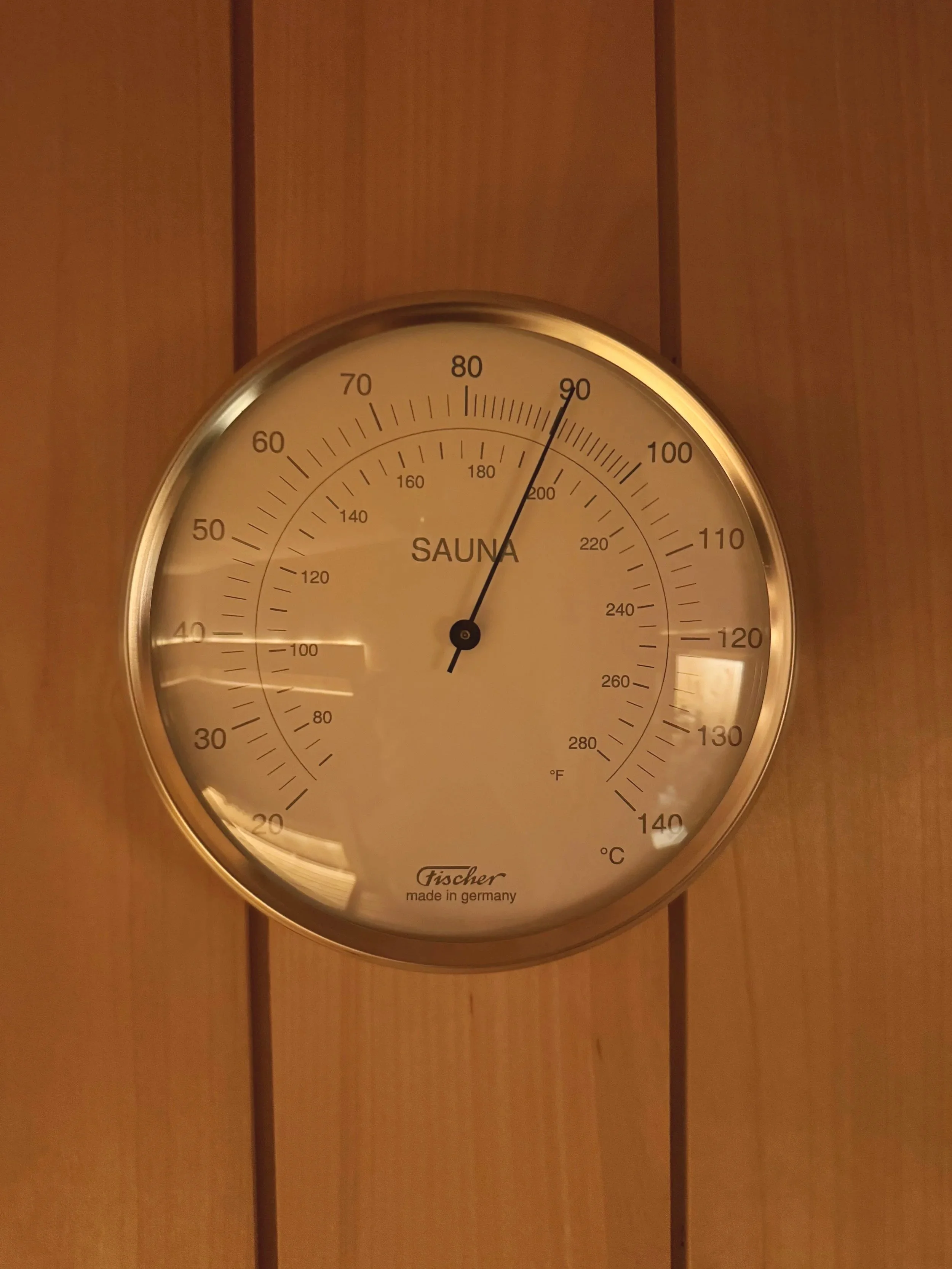 Thermometer on wooden wall, showing 90°F, 30°C, and 32°C, indicating temperature, with the word 'SAUNA' written in the center.