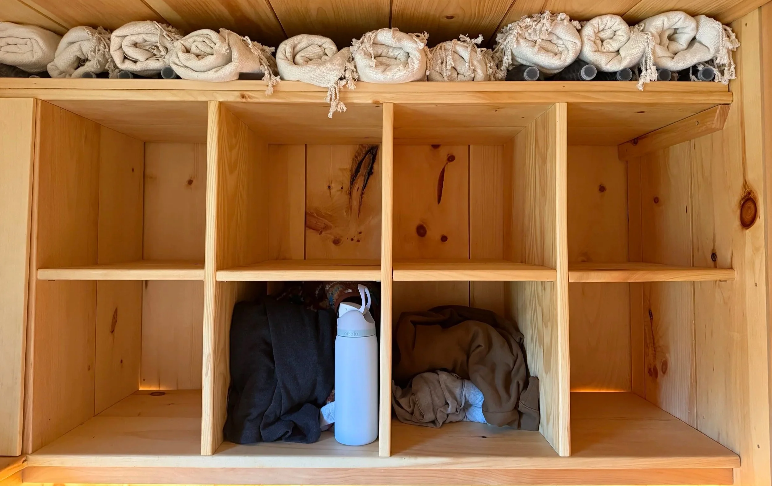 Empty wooden cubbies with a few clothes and a white water bottle at the bottom.