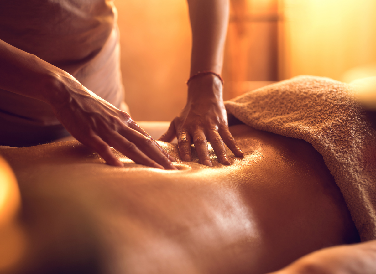 Person receiving a back massage with oils in a dimly lit room.