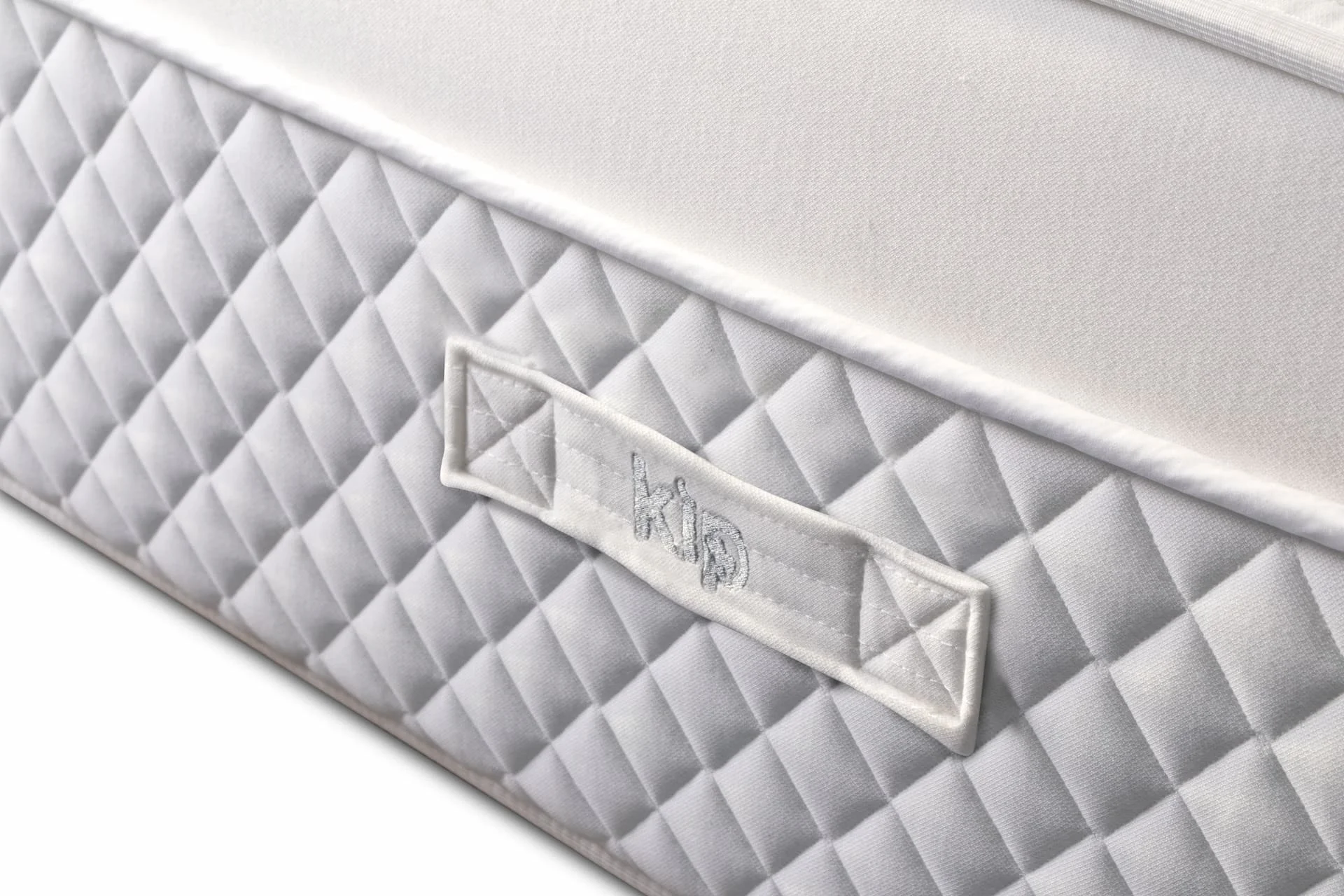 Close-up of a white quilted mattress with a fabric tag that has the brand name 'KID' embroidered on it.