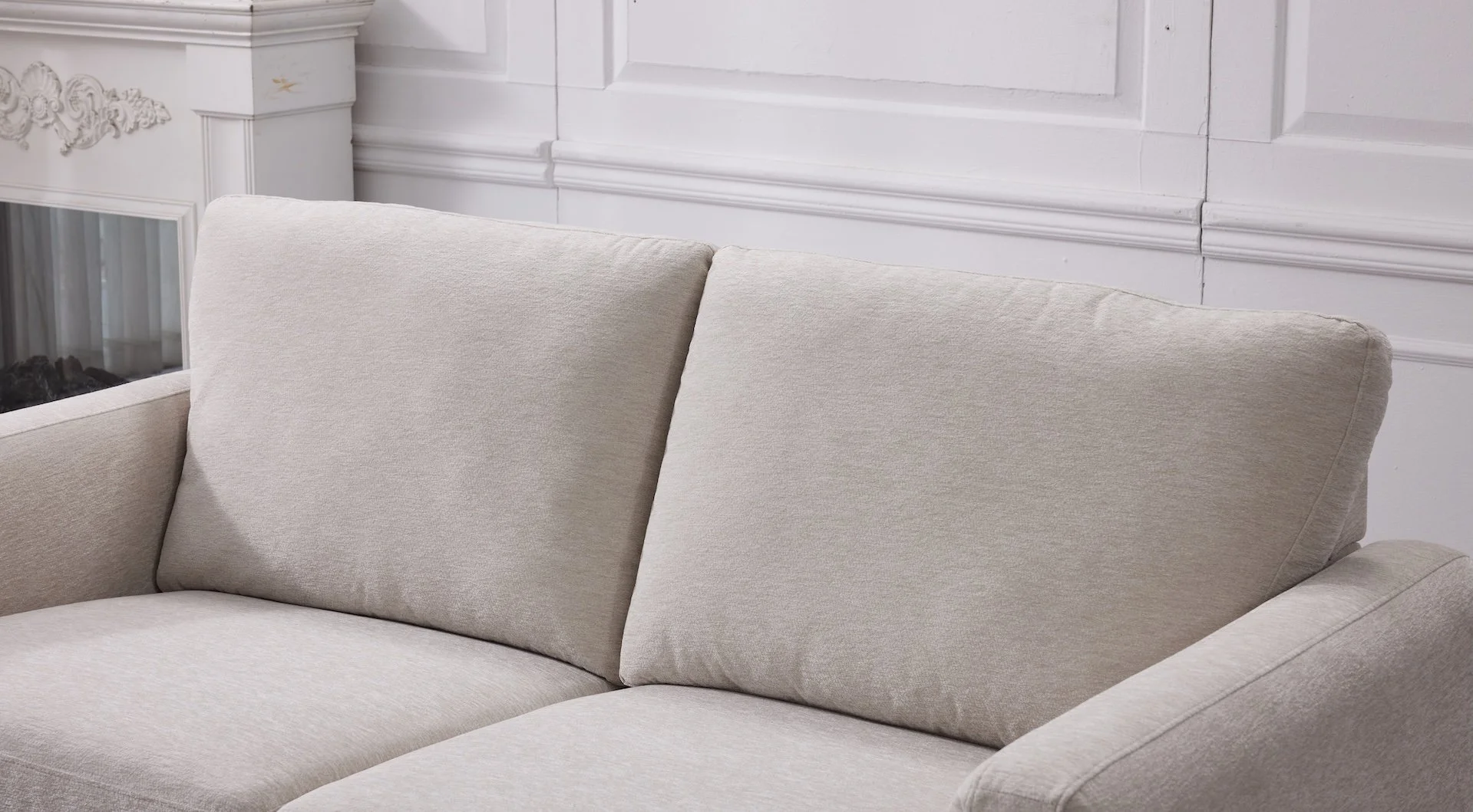 Close-up of a light beige upholstered sofa with a cushioned backrest, situated in a room with white paneled walls.