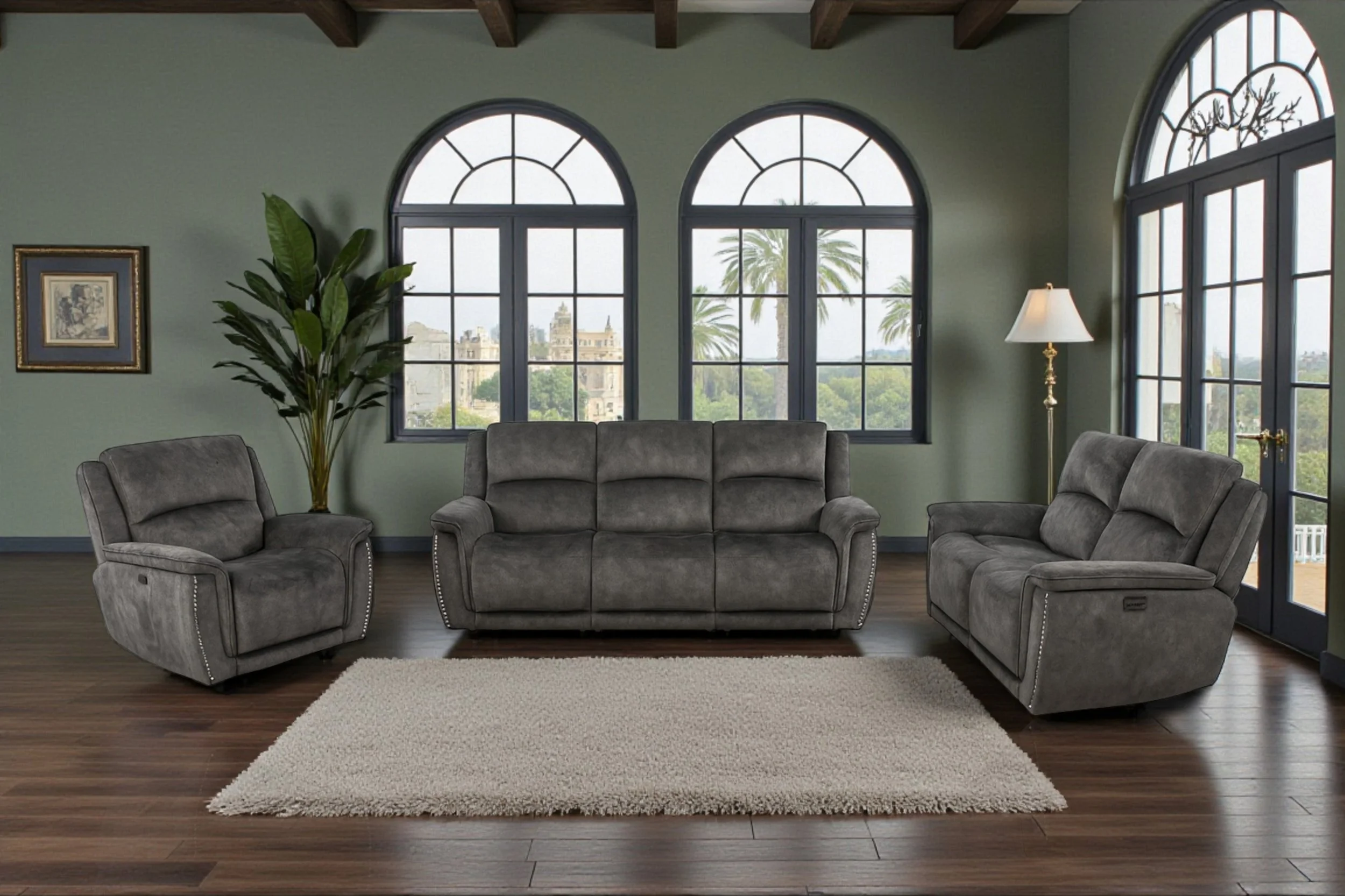 A modern living room with a white wall, large windows with sheer curtains, and dark hardwood floors. There is a dark gray three-seater sofa and two matching armchairs arranged around a beige area rug. A framed abstract art piece hangs on the wall above the sofa.
