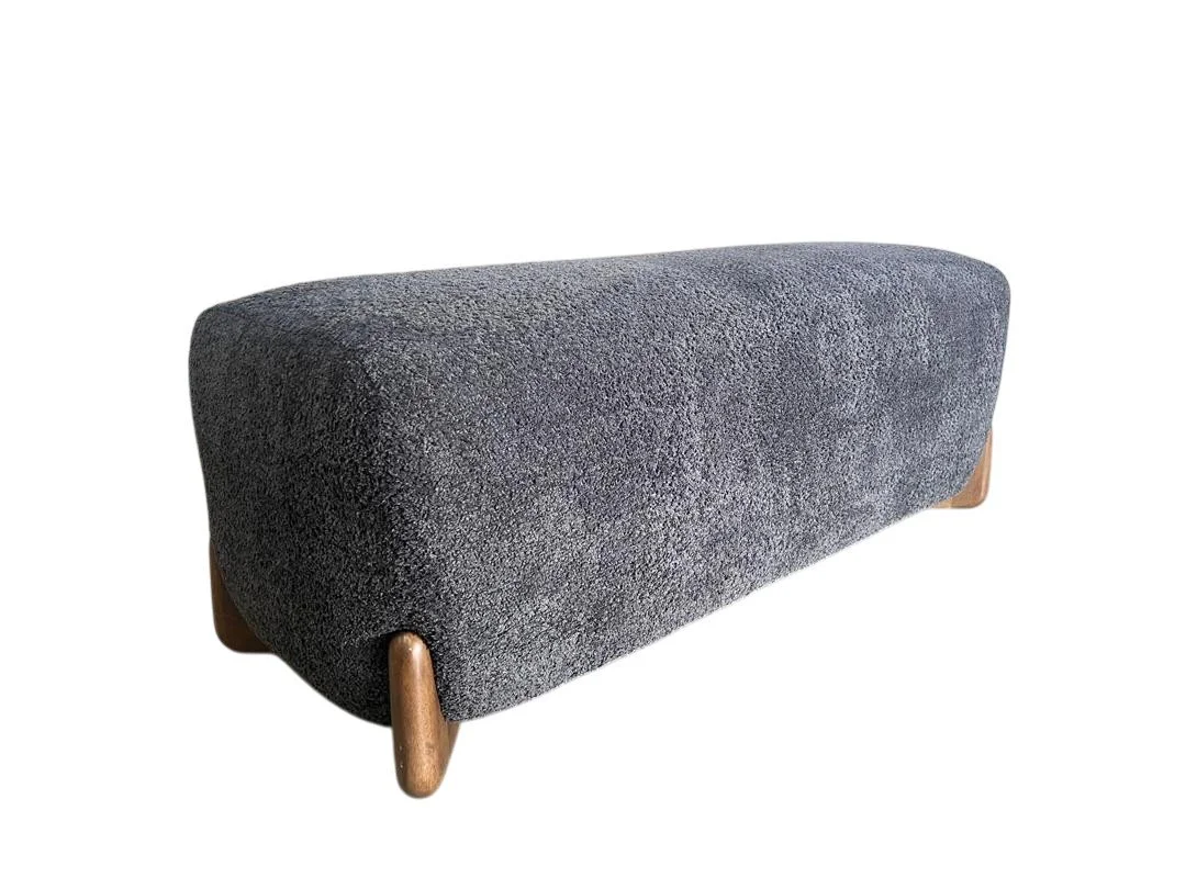 A long, upholstered, dark gray fabric bench with wooden legs.