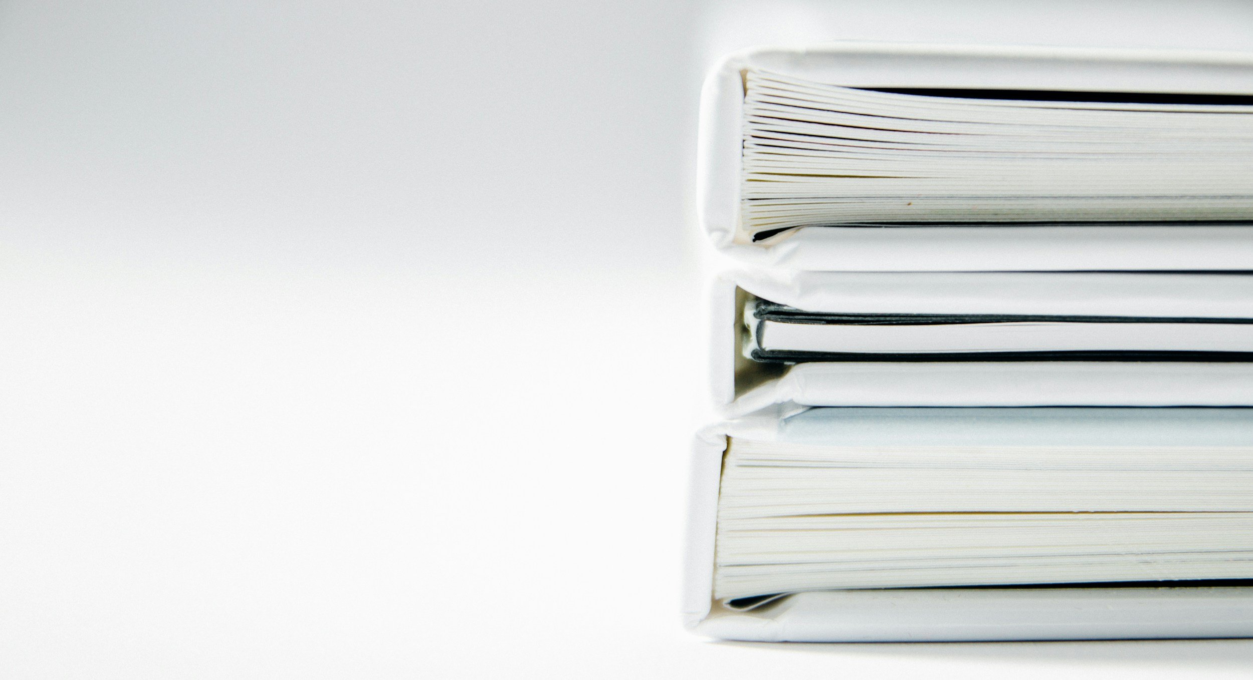 Stack of five white binders or notebooks with paper inside, arranged horizontally on a white surface.