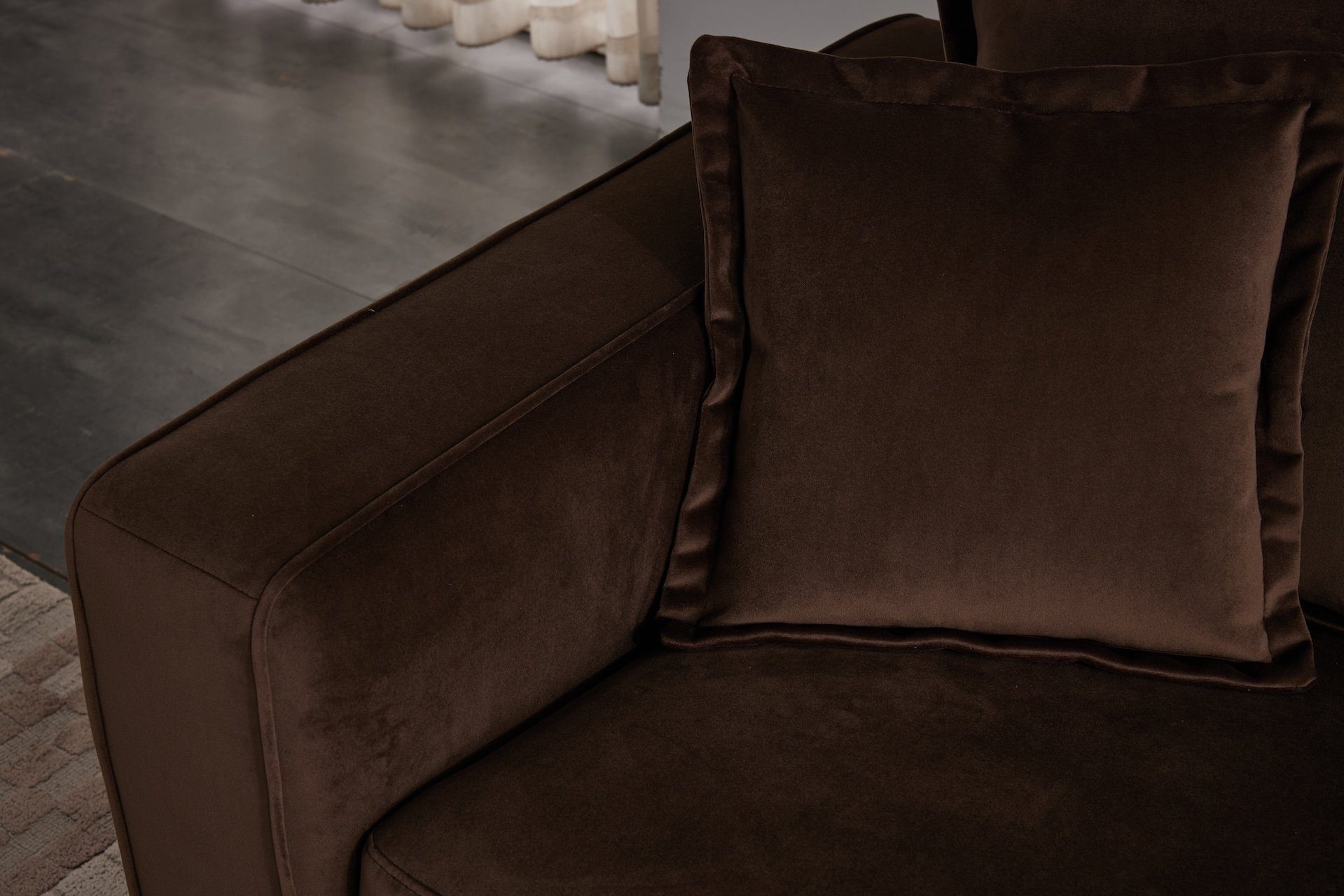 Close-up of a brown velvet sofa with pillows, showing the armrest and part of the seating area.
