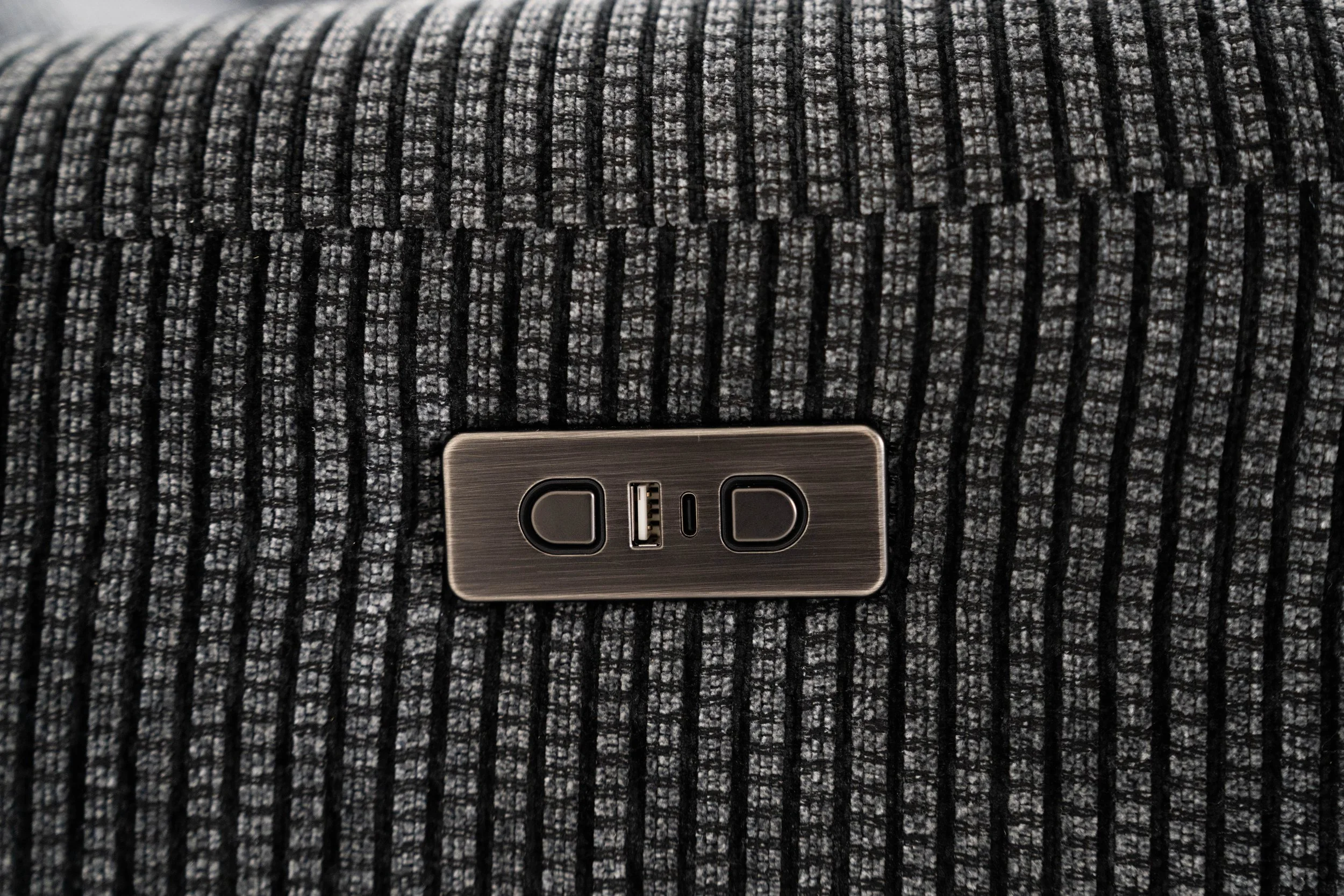 Close-up of a power outlet with USB port on a textured, patterned fabric surface.