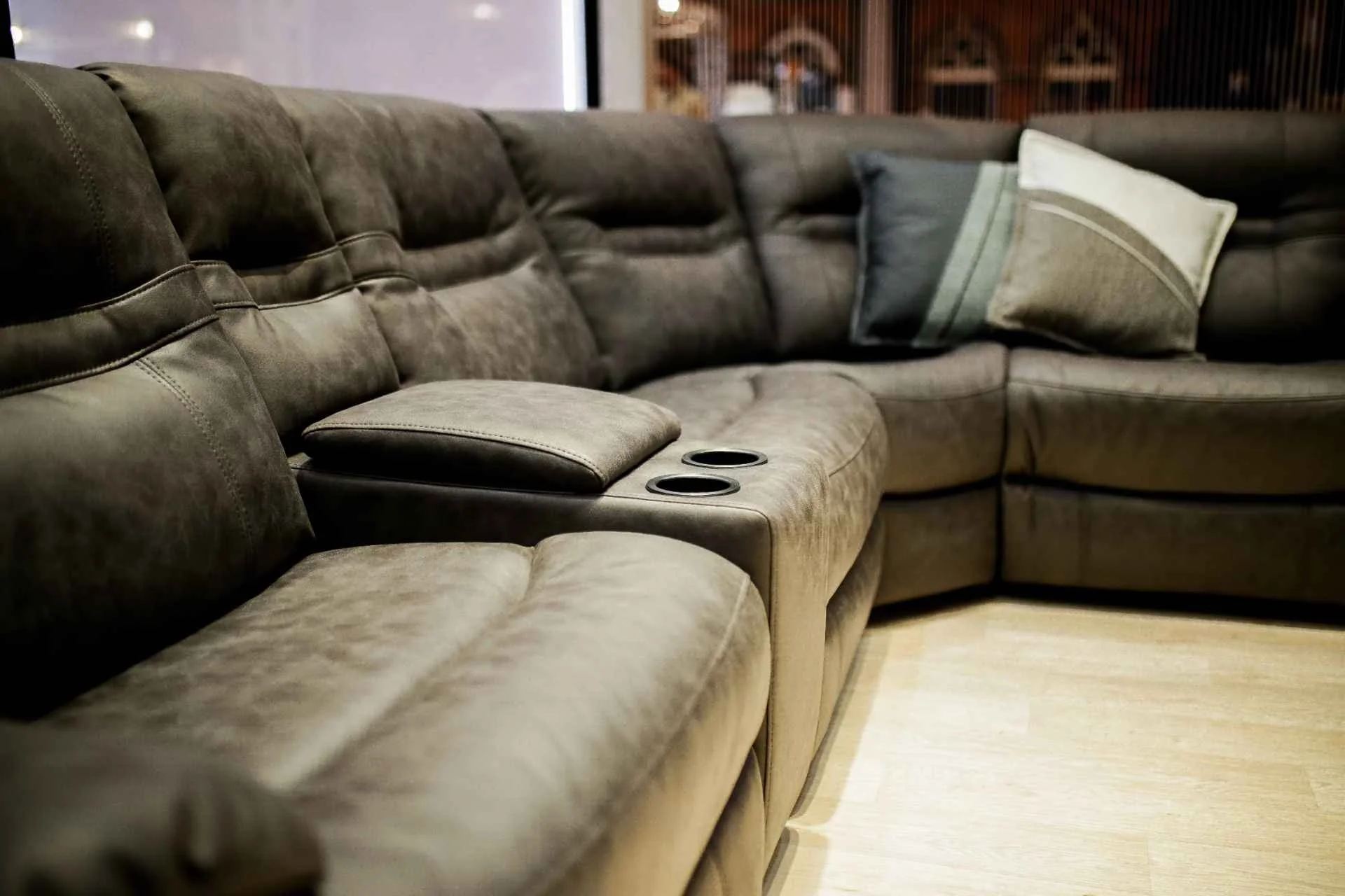 A large L-shaped brown sectional sofa with built-in cup holders and two decorative pillows in a living room.