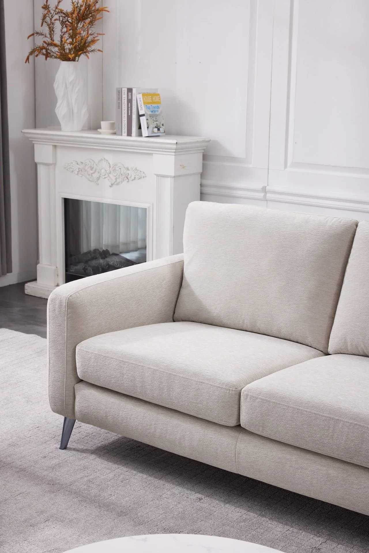 A beige sofa in a living room with a white decorative fireplace and a white rug.