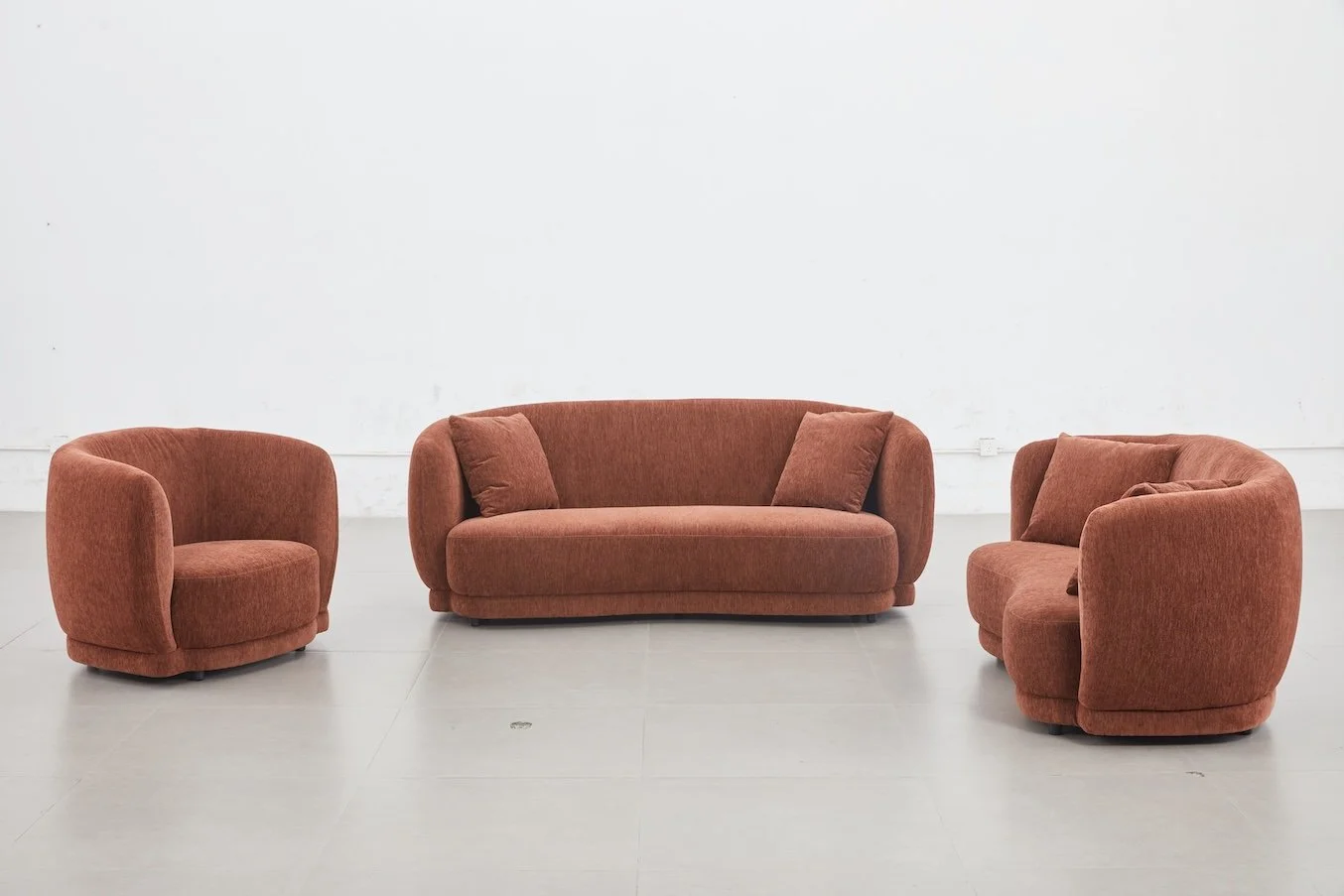 Set of three rust-colored upholstered sofas and armchairs arranged facing each other in a plain white room.