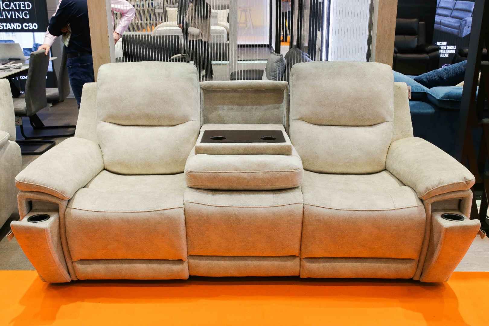 Cream-colored sectional sofa with built-in cup holders and a center storage compartment, displayed on an orange floor at a furniture store.