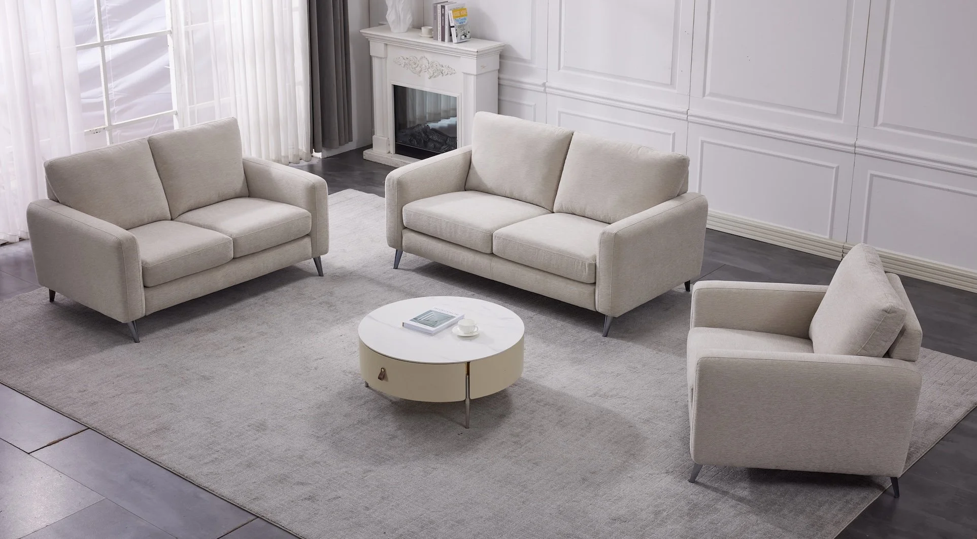 Living room with beige sofas, a round white coffee table, a white rug, a fireplace, and large windows with curtains.