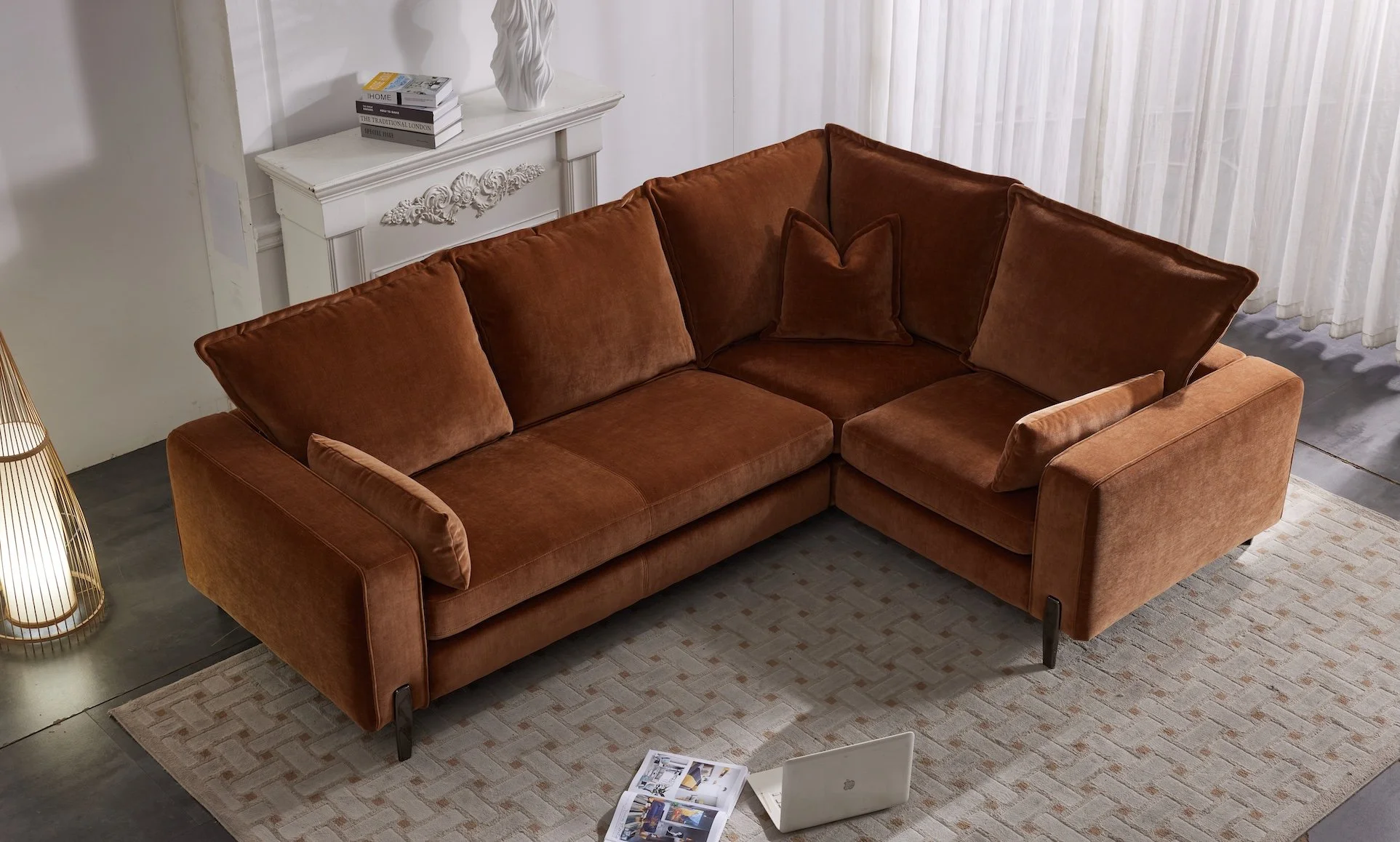 A burnt orange sectional sofa with cushions in a living room next to a beige patterned rug, a laptop, and an open magazine on the floor.