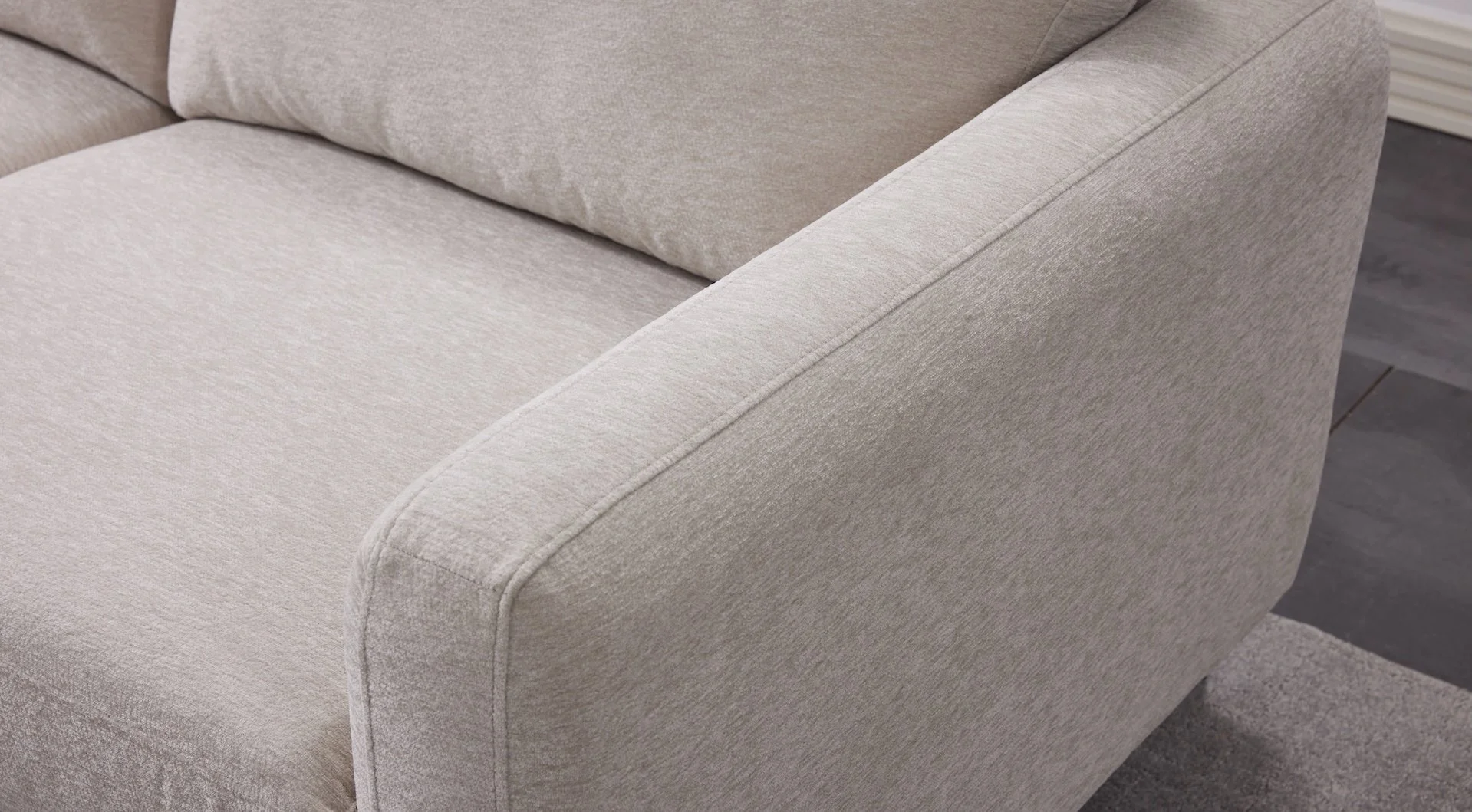 Close-up of a beige upholstered sofa arm and cushion with textured fabric, on a dark wooden floor.