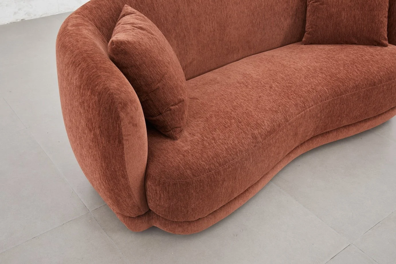 A close-up of a red-orange upholstered sofa with curved armrests and matching cushions on a light-colored tiled floor.